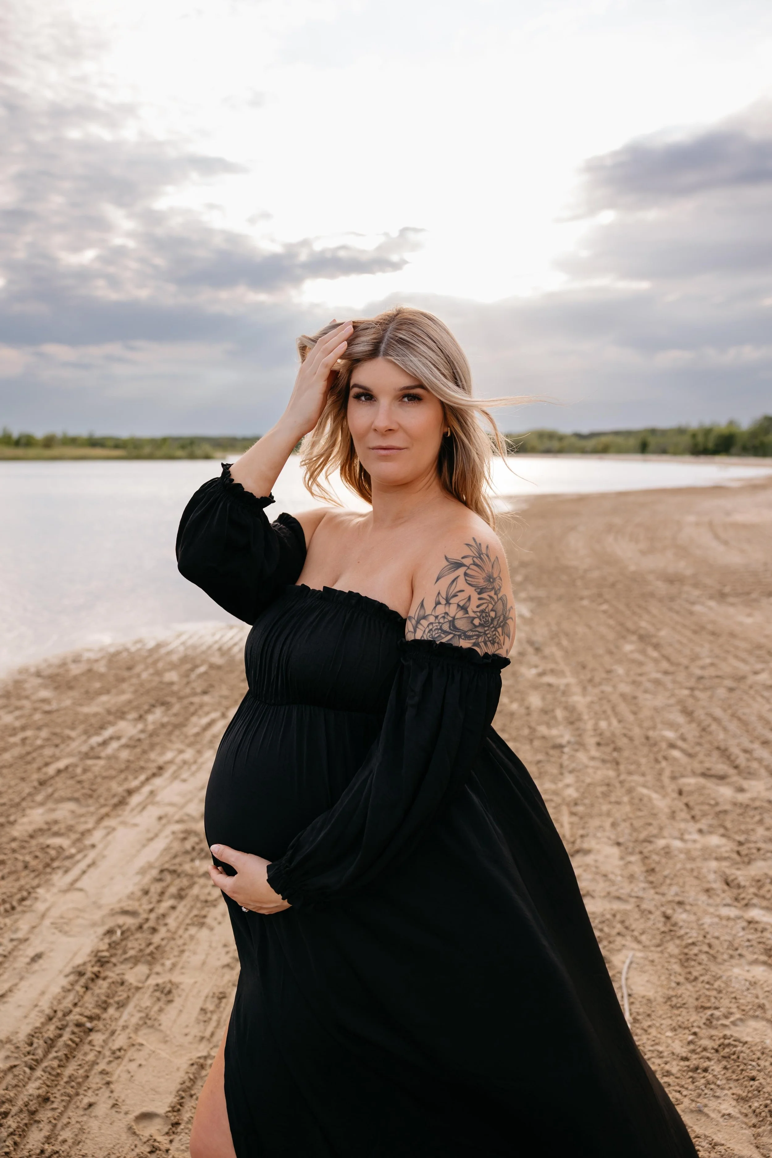 A pregnant woman standing on a sandy beach in winnipeg at maternity session with sari Risbey photography