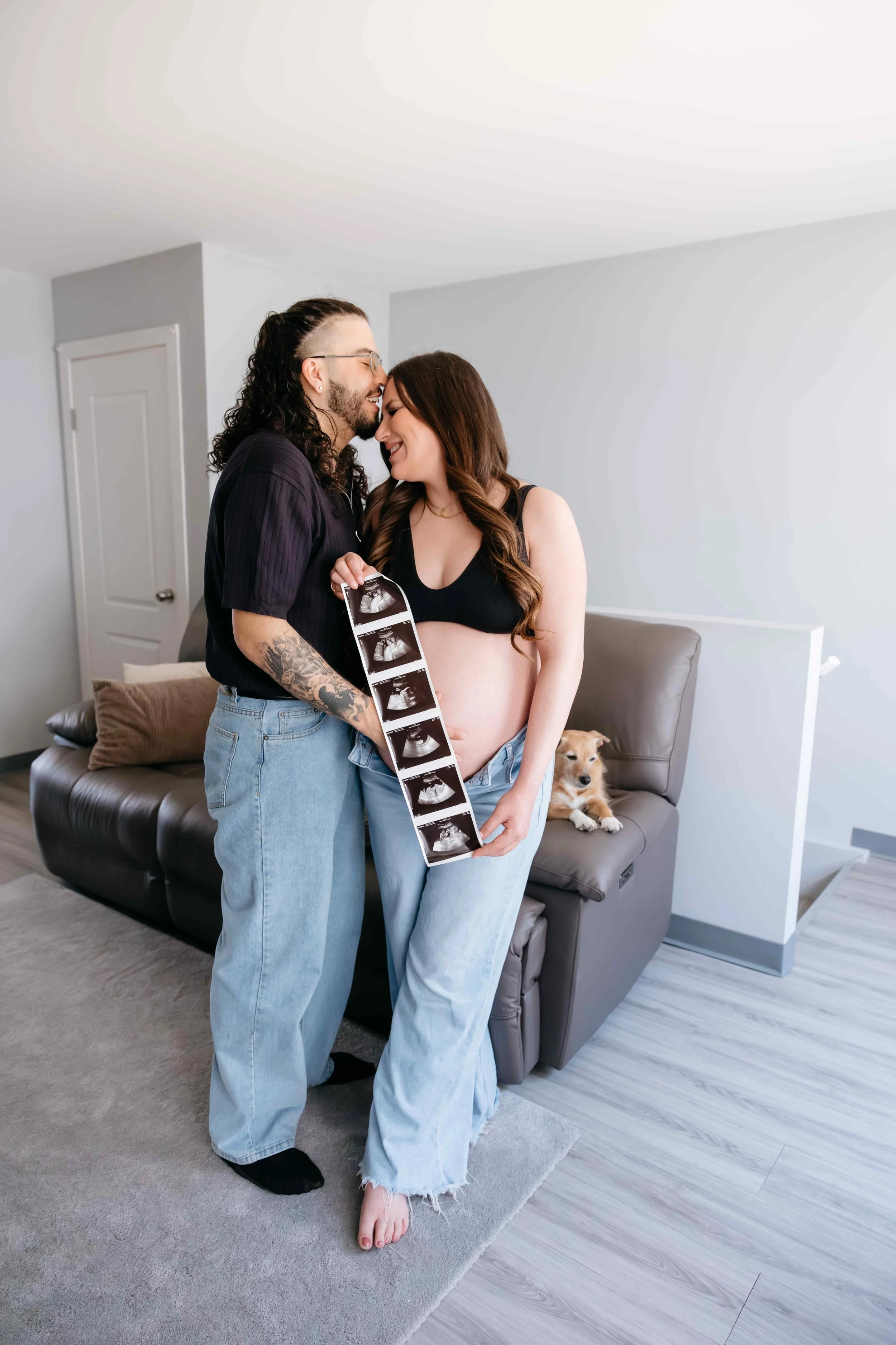 A couple standing close together indoors, holding ultrasound scan images at a maternity session in Winnipeg