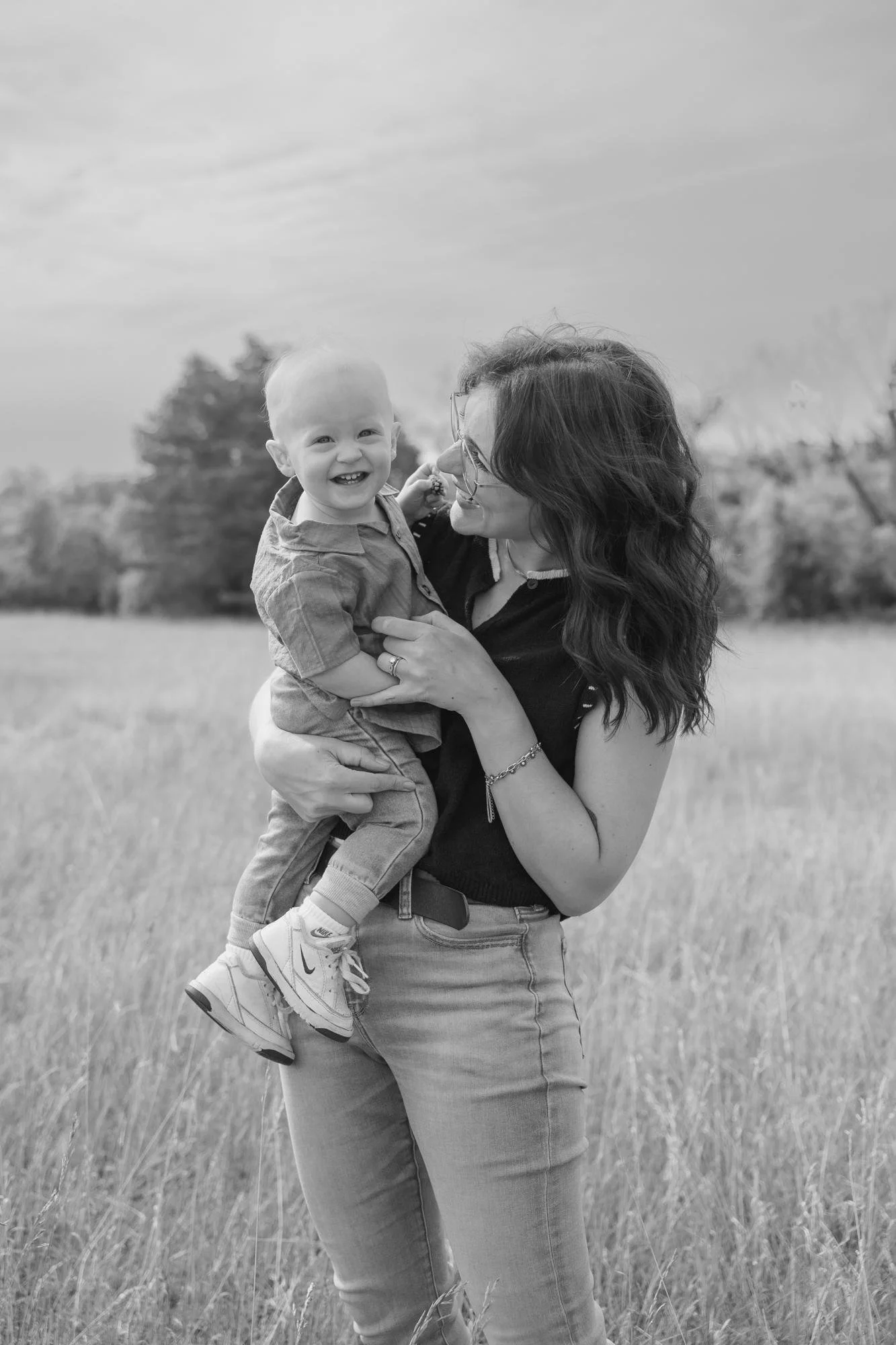 A mom holding a young boy with a big smile in an outdoor field at a family session with Sari Risbey, Winnipeg family photography
