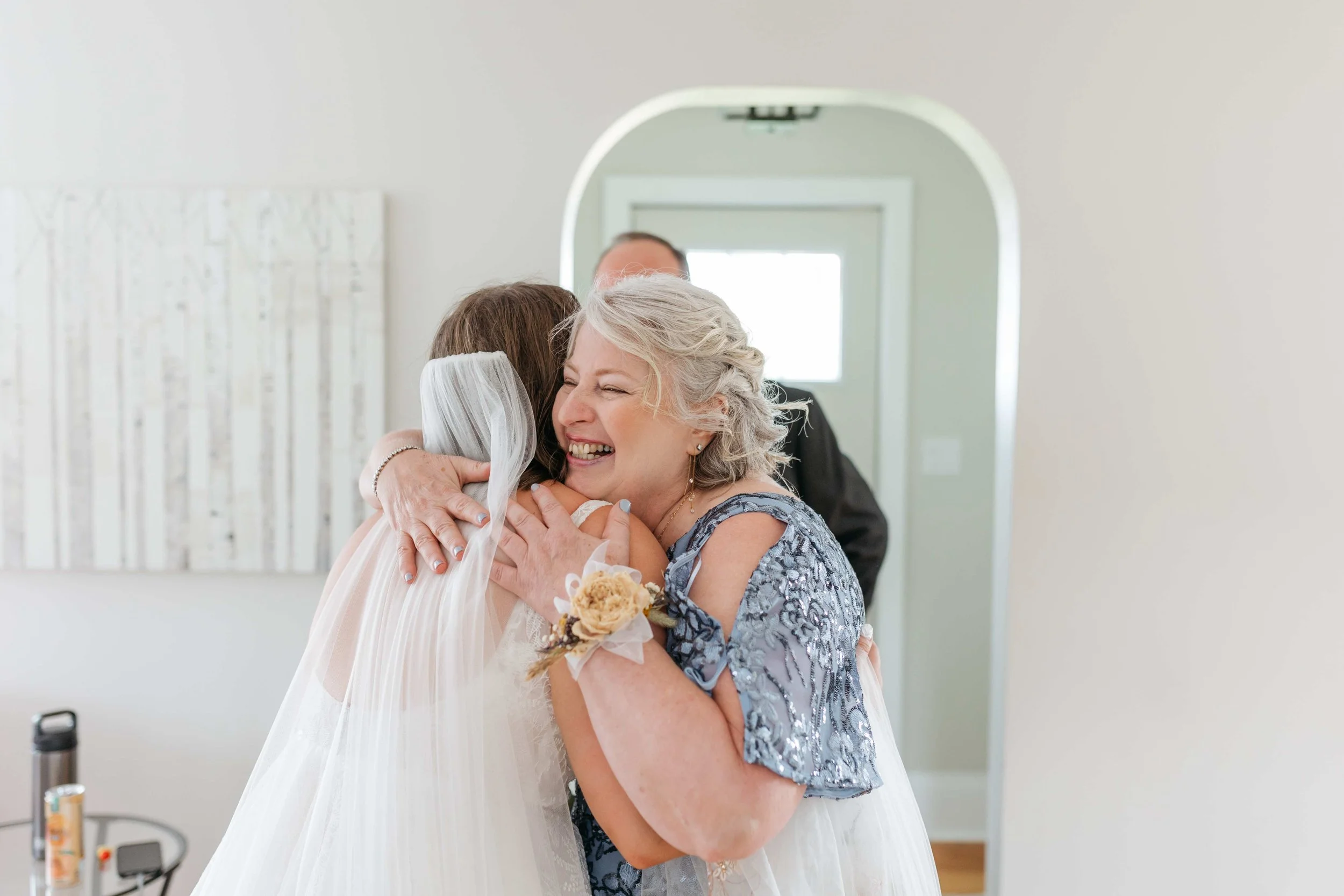 An elderly woman with gray hair hugging a woman in a wedding dress during a heartfelt moment at a wedding celebration.