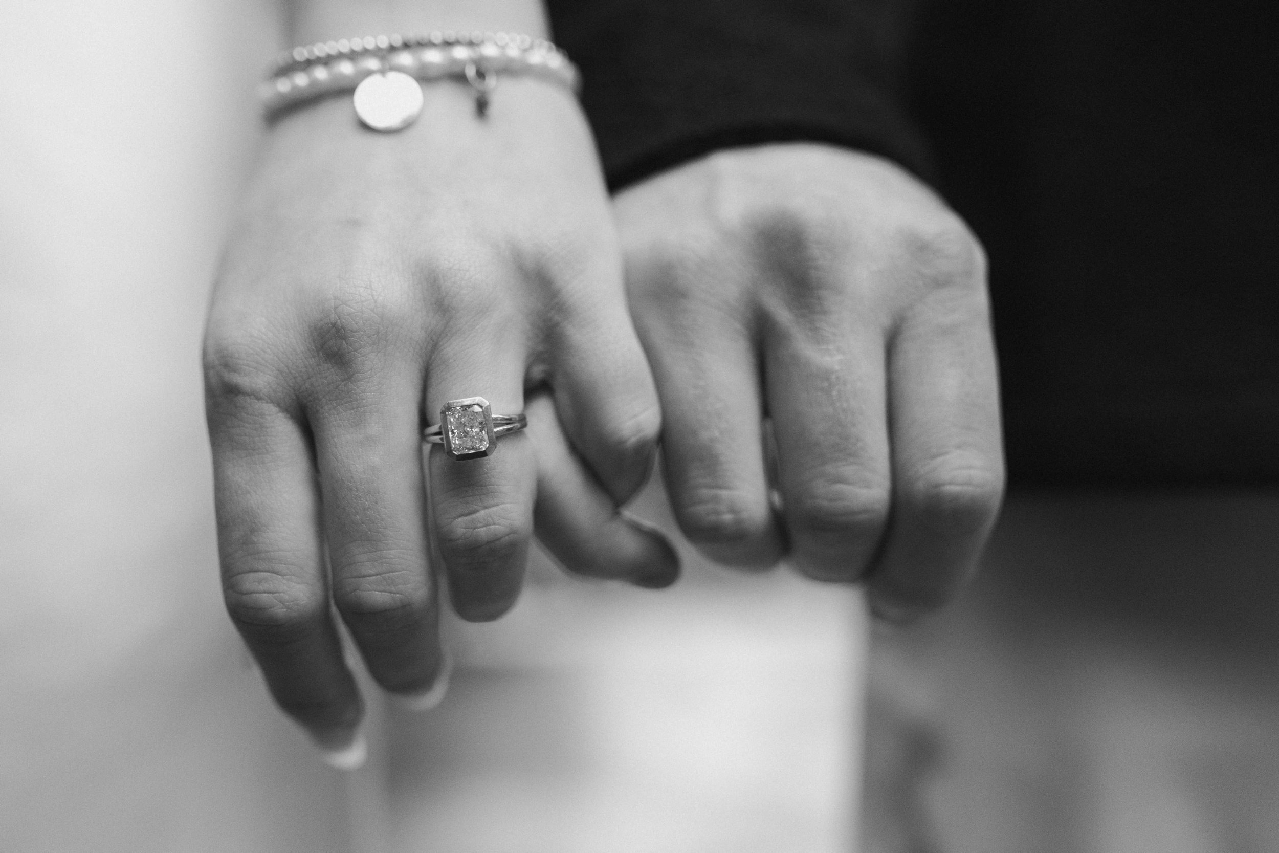Close-up of a person's hand with a ring on the ring finger, and a couple of bracelets on the wrist, holding another person's hand in black and white.