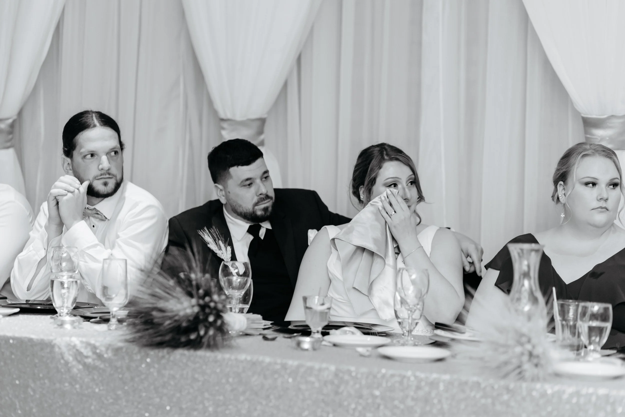 People sitting at a decorated table during a formal event, with curtains in the background.