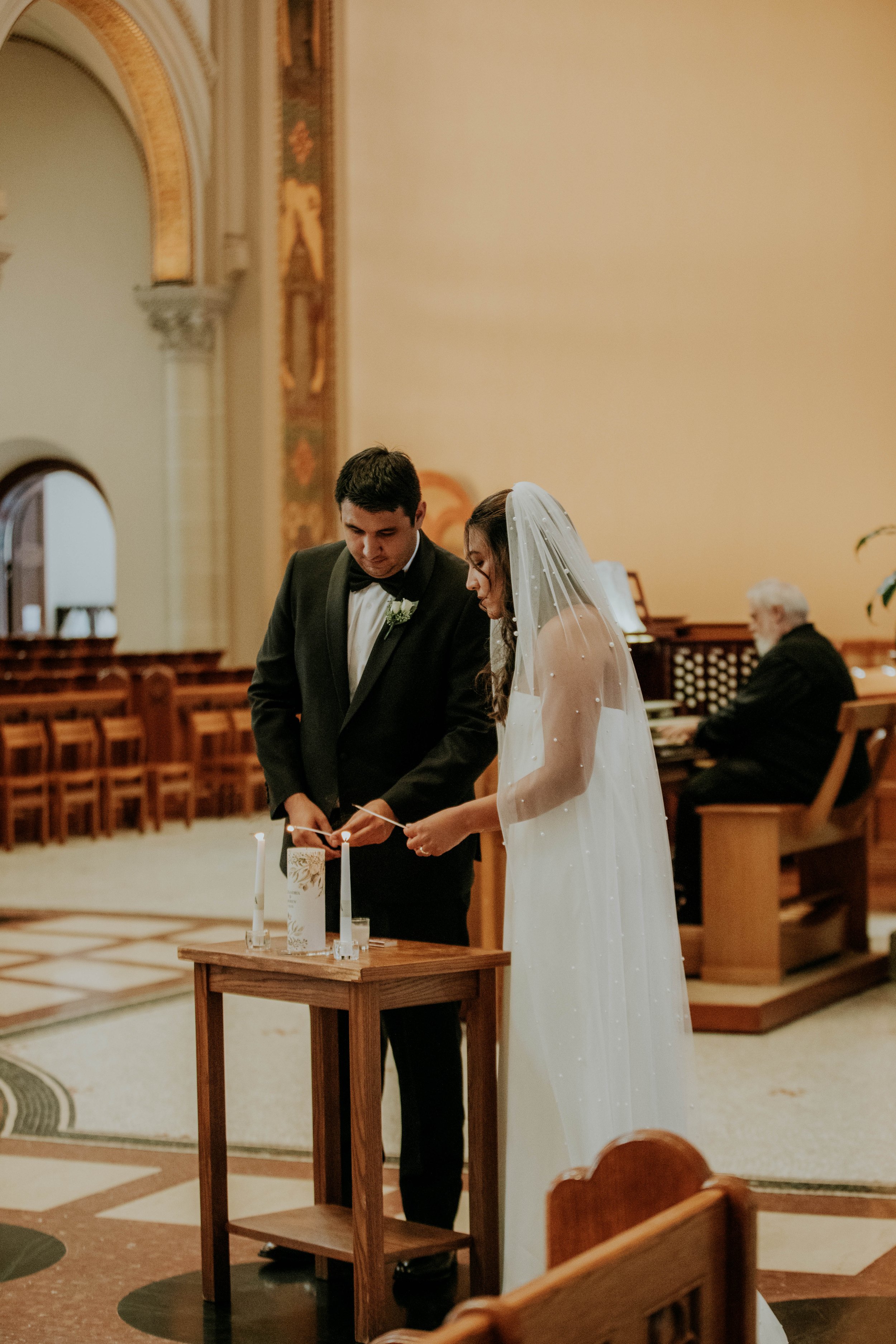 A bride and groom lighting candles during a wedding ceremony inside a church.