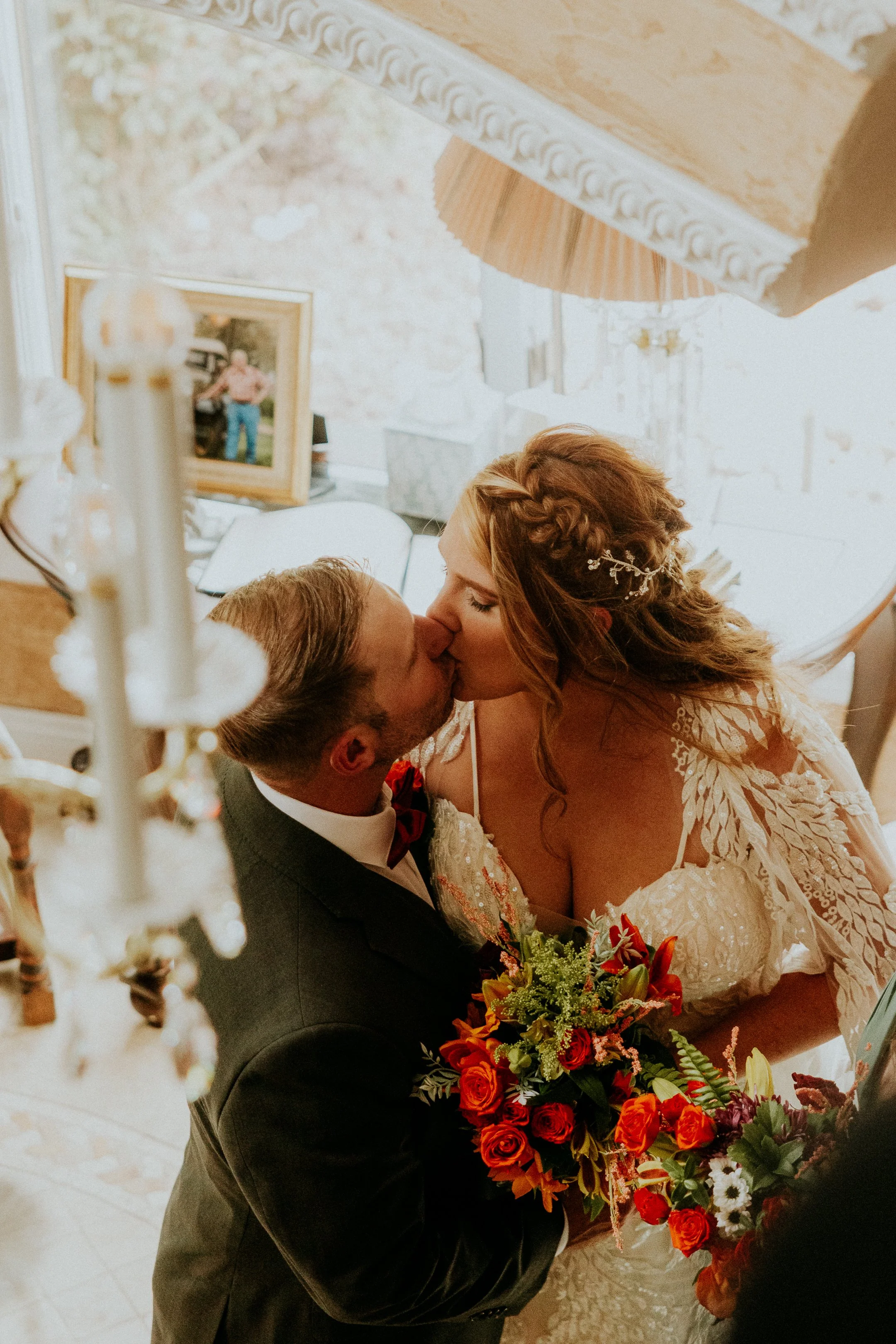 A bride and groom sharing a kiss during their wedding ceremony, with the bride holding a bouquet of vibrant red, orange, yellow, and white flowers.