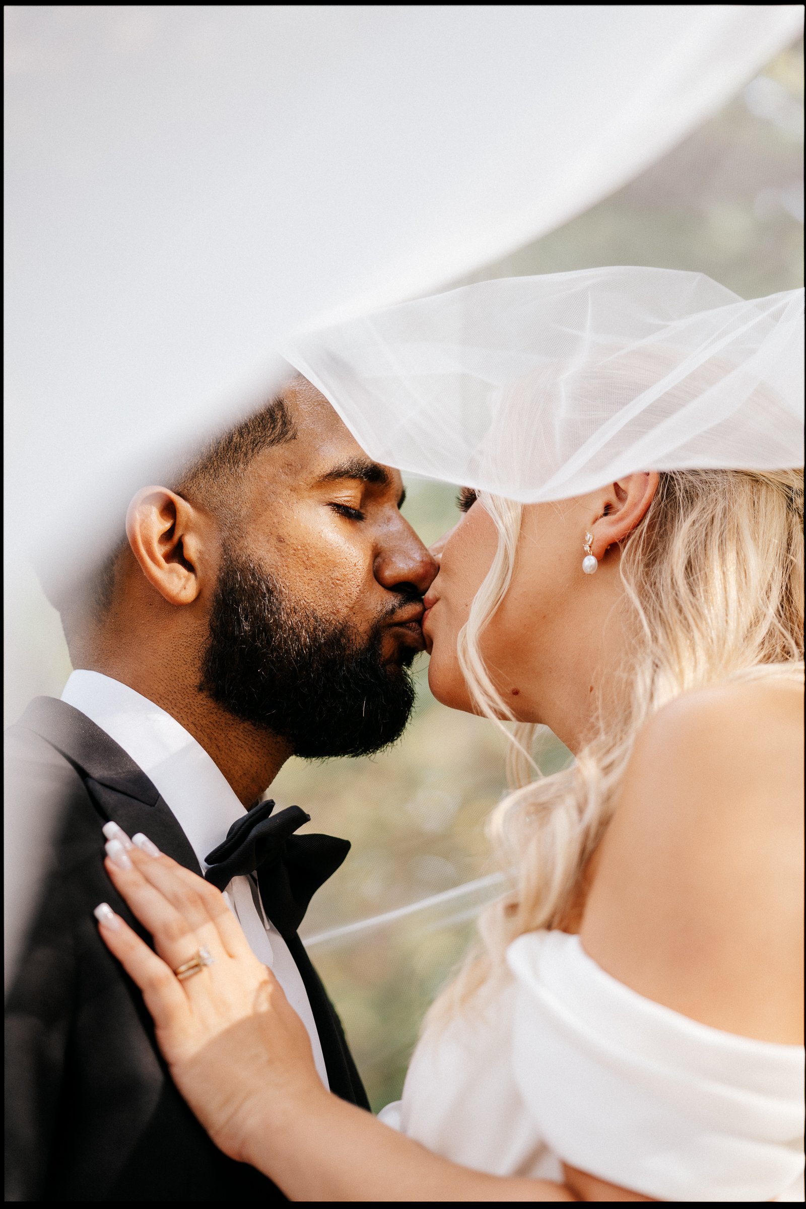 A close-up of a bride and groom touching foreheads with eyes closed, sharing an intimate moment during their wedding, with the bride wearing a white dress, pearl earrings, and a veil, and the groom in a black tuxedo with a bow tie.