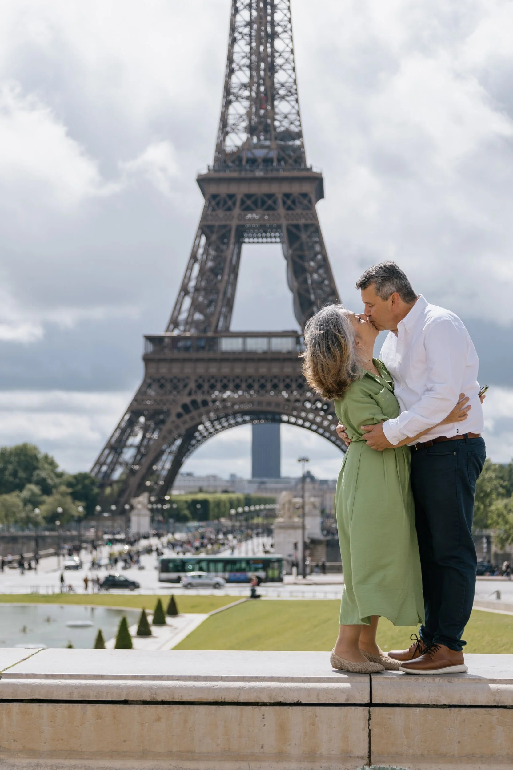 A couple kissing in front of the Eiffel Tower in Paris, France, with the city and a busy street visible below.