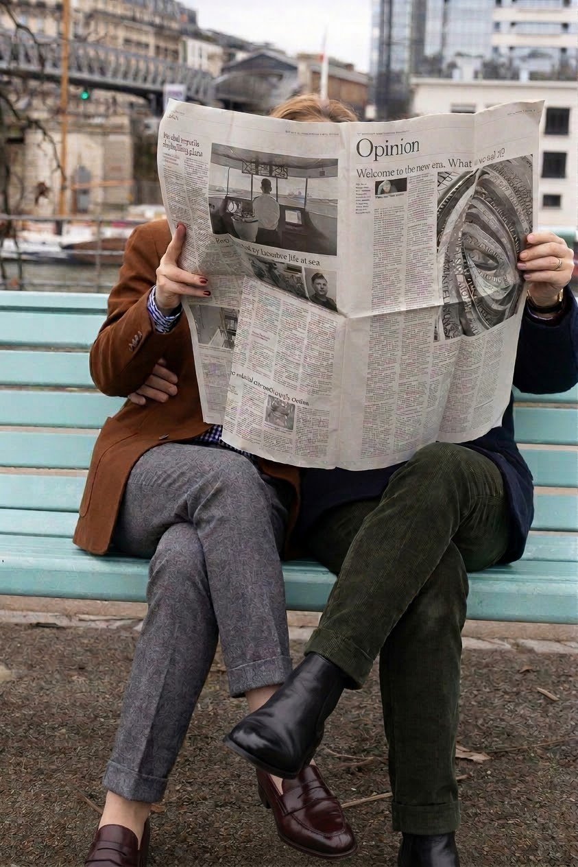Two people sitting on a light blue park bench reading a newspaper covered faces, with an urban cityscape in the background.