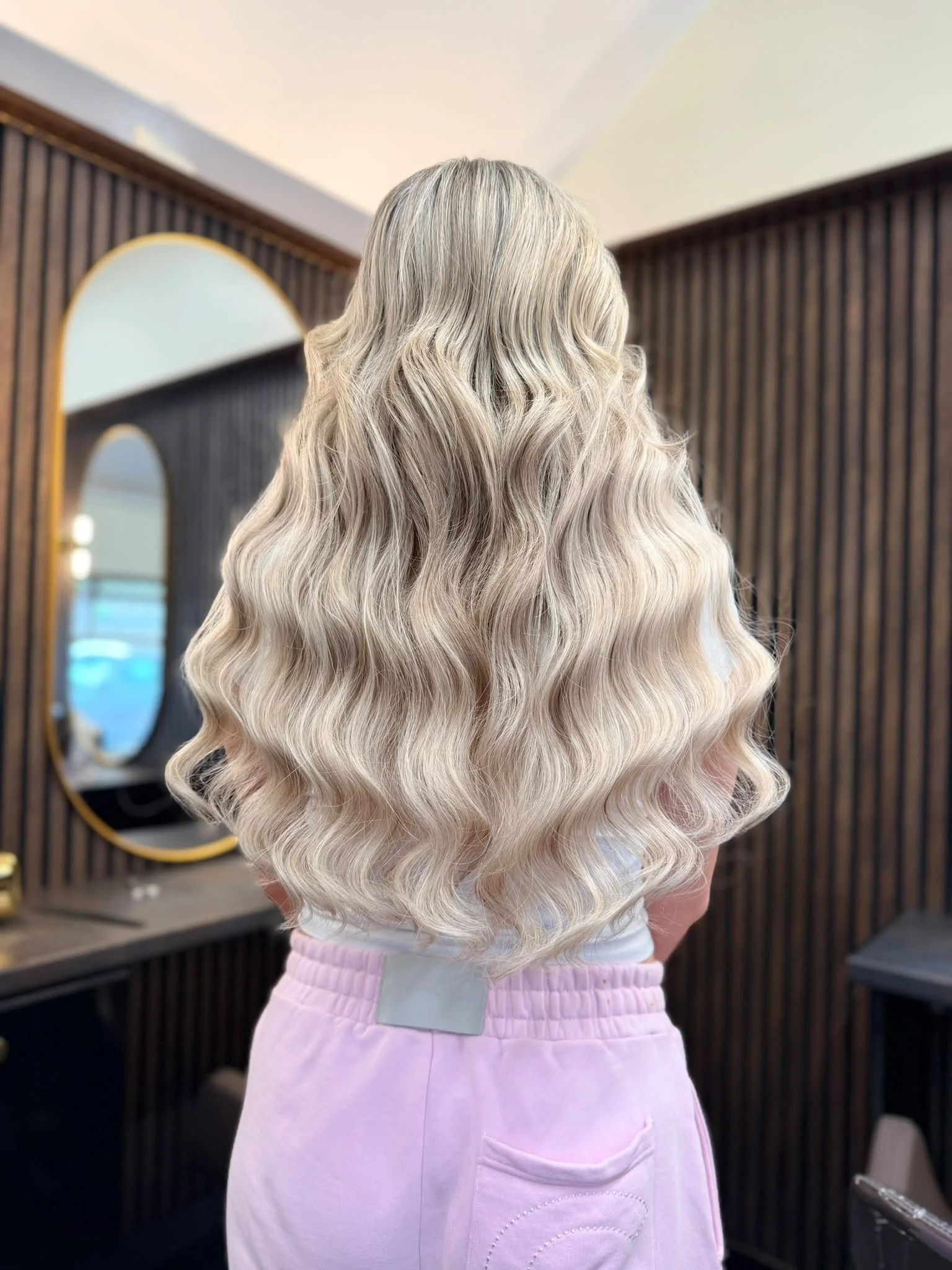 Back view of long, voluminous platinum blonde hair styled in loose waves at a salon