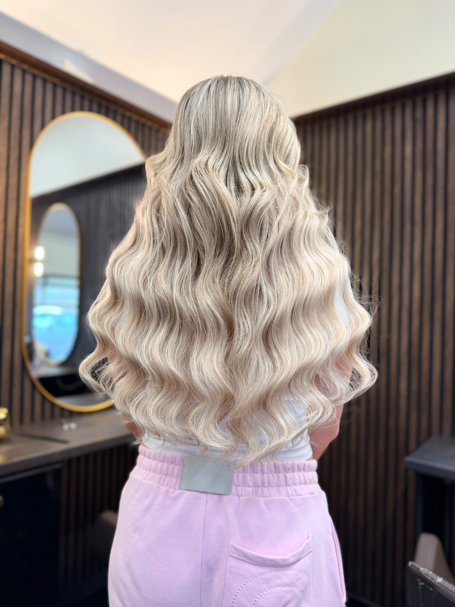 Back view of long, voluminous platinum blonde wavy hair in a salon