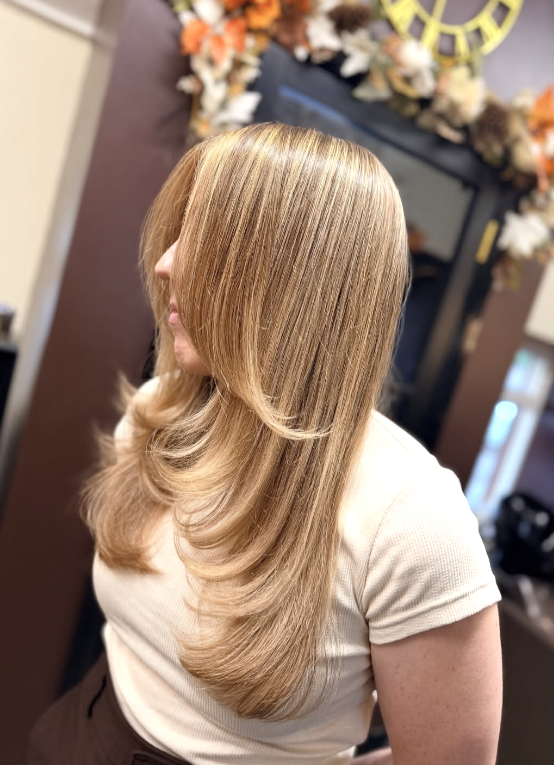 Woman with long honey-blonde layered hair and side-swept curtain bangs in a salon