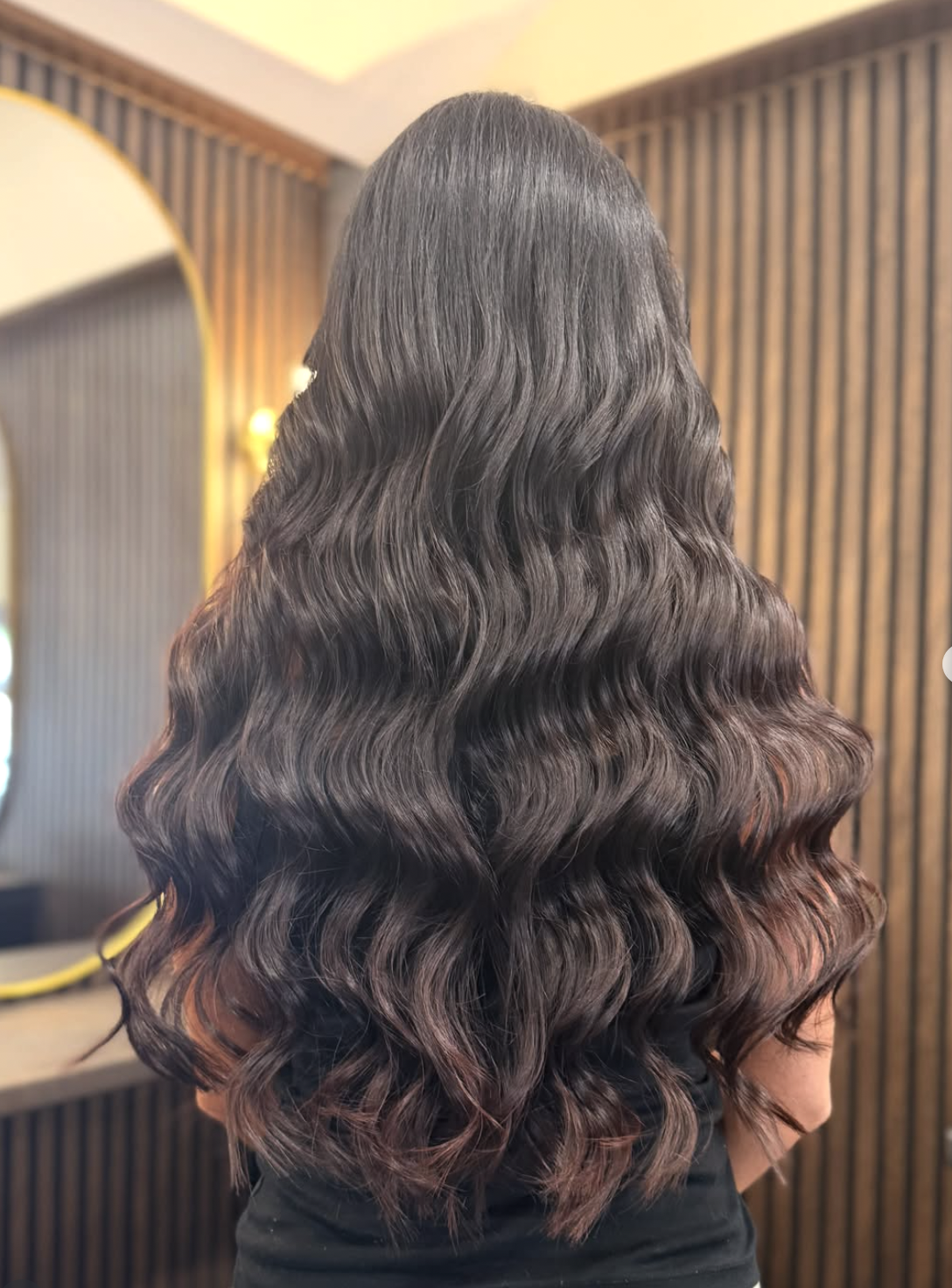 Back view of long, voluminous dark brown wavy hair with soft curls in a salon