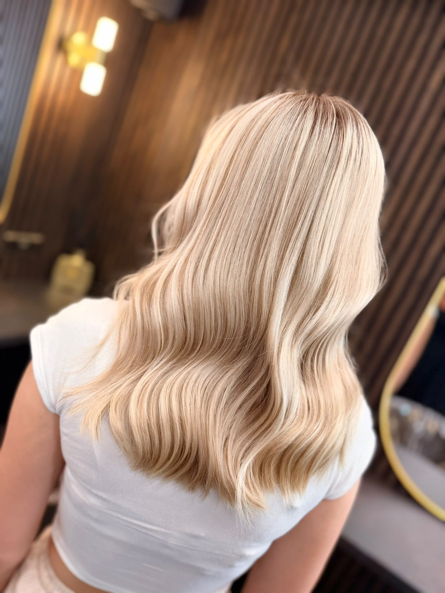 Back view of a woman with long, wavy platinum blonde hair in a salon.