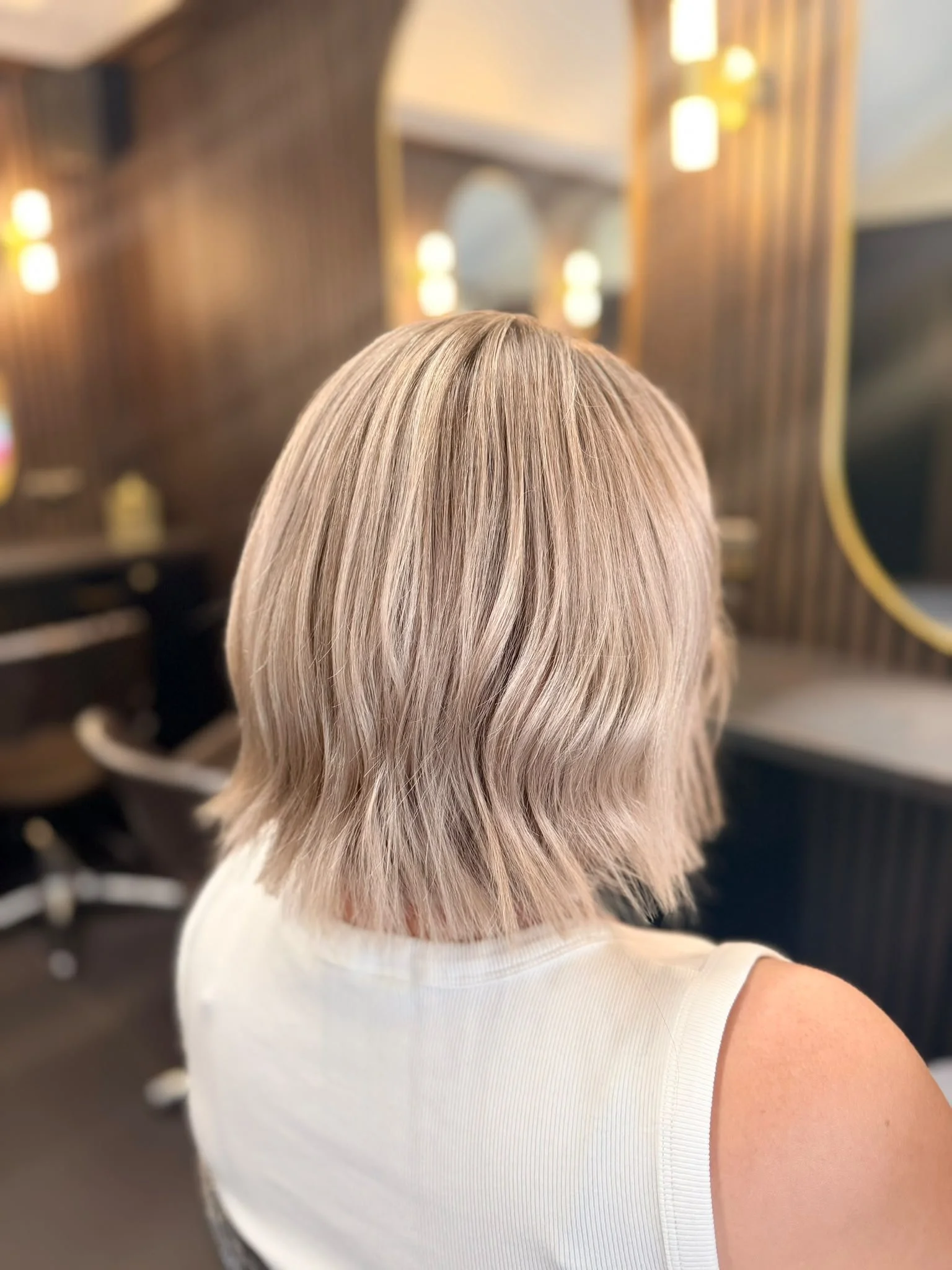 Back view of a woman with shoulder-length ash blonde layered hair in a salon chair