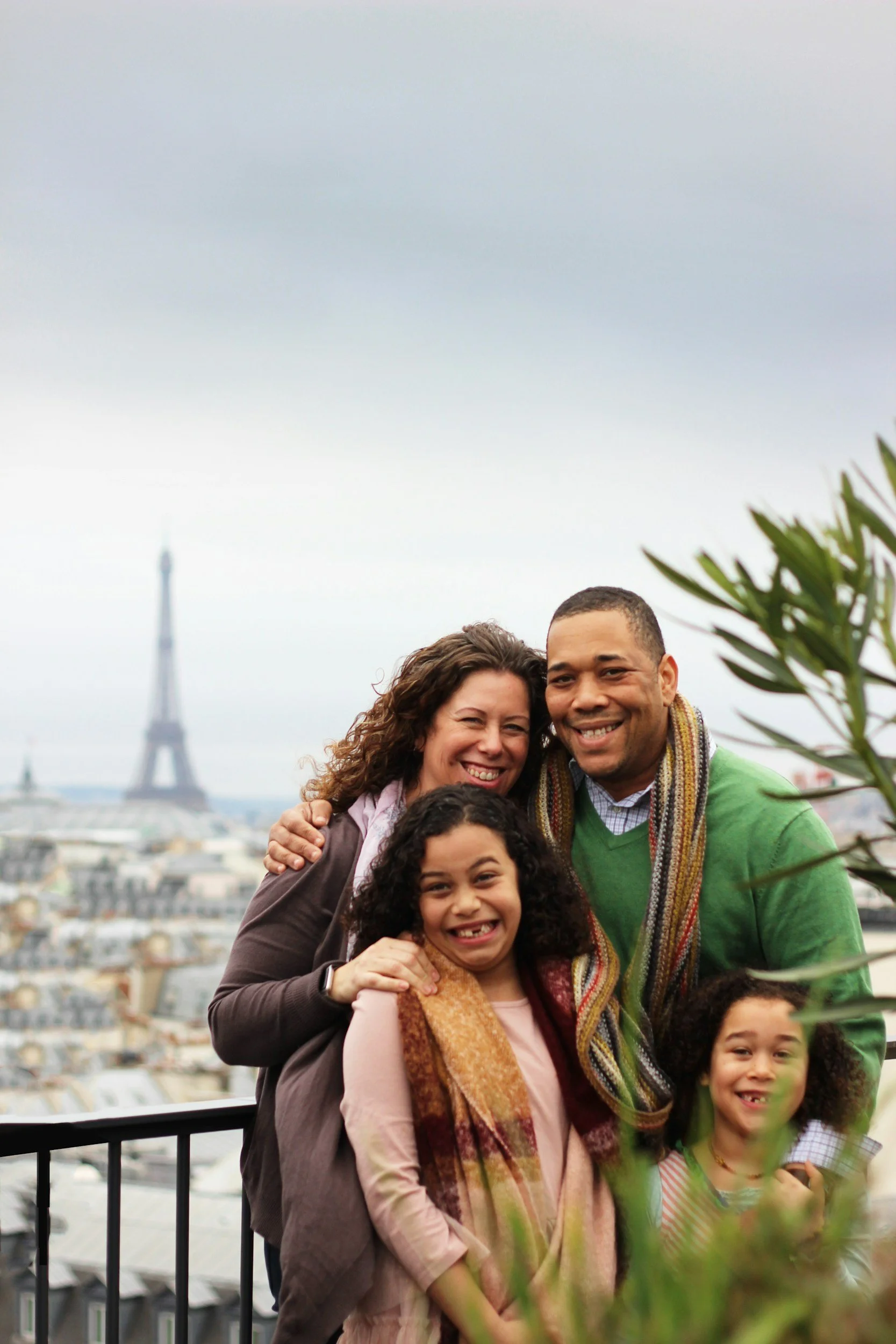 A group of six people smiling at the camera with the Eiffel Tower in the background, on a cloudy day in Paris.