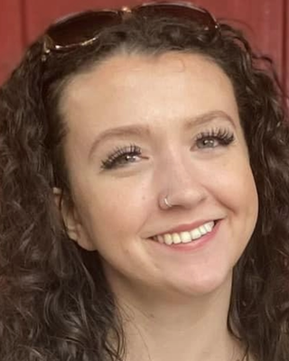 Close-up of a smiling young woman with curly hair, wearing glasses on her head, and a nose piercing.