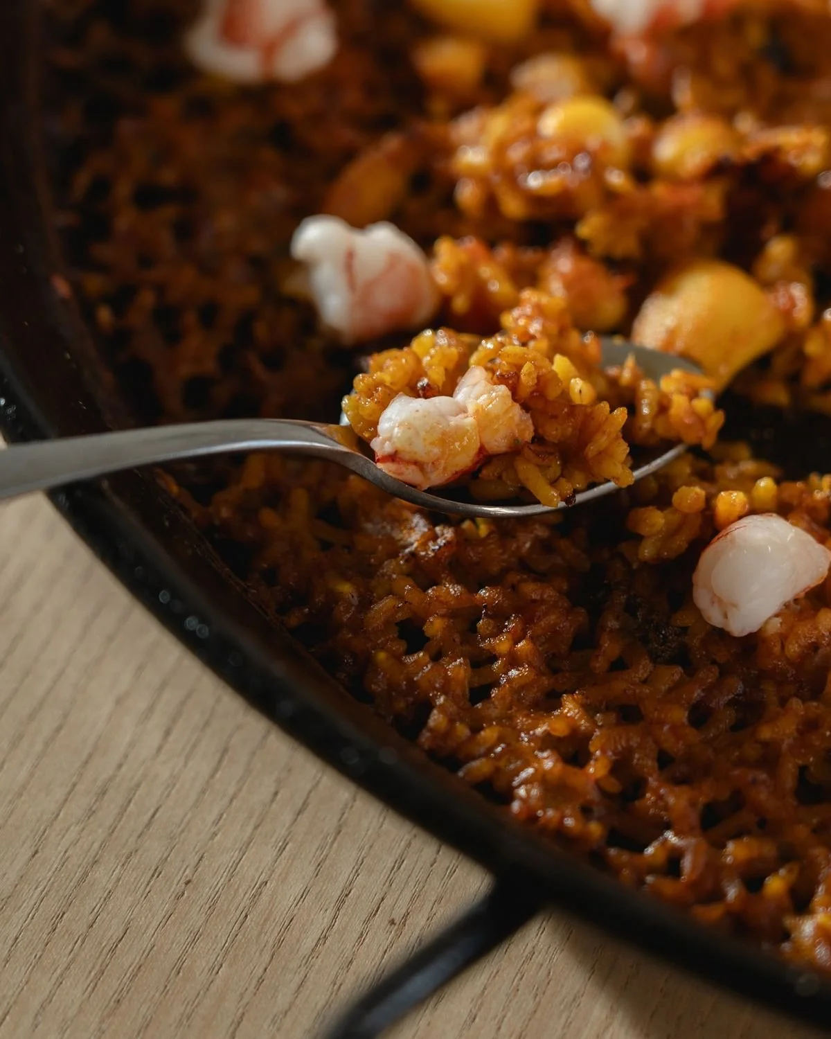 Un sartén con arroz frito con camarones y otros ingredientes, con una cuchara sirviendo una porción.