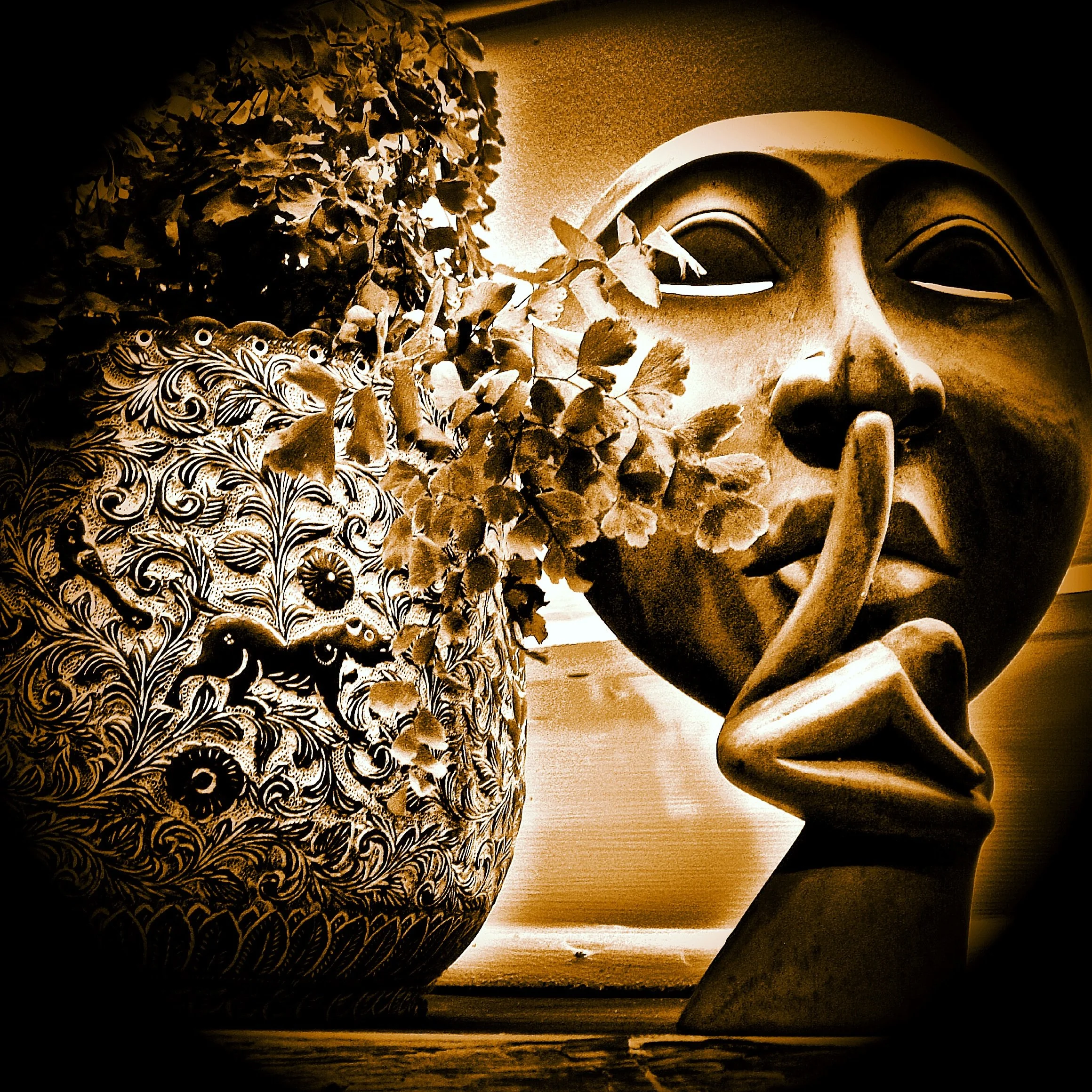 Close-up of a carved and painted mask with intricate detailing, surrounded by dried leaves, with a dark background.