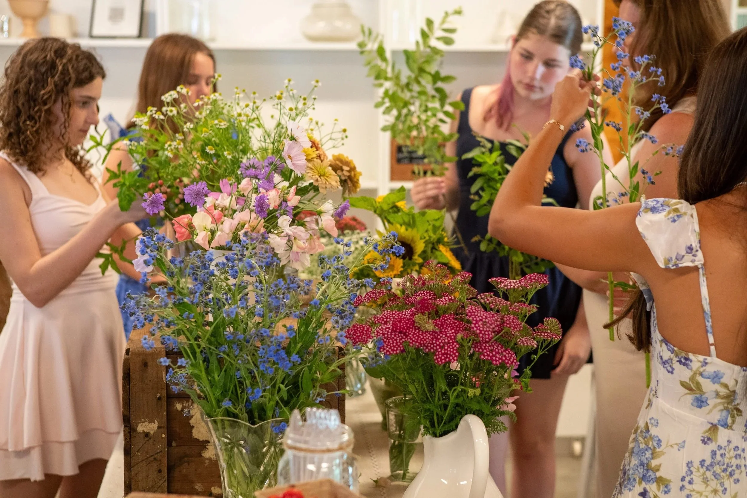 Group of women selecting flowers at a flower shop, with colorful bouquets on display.
