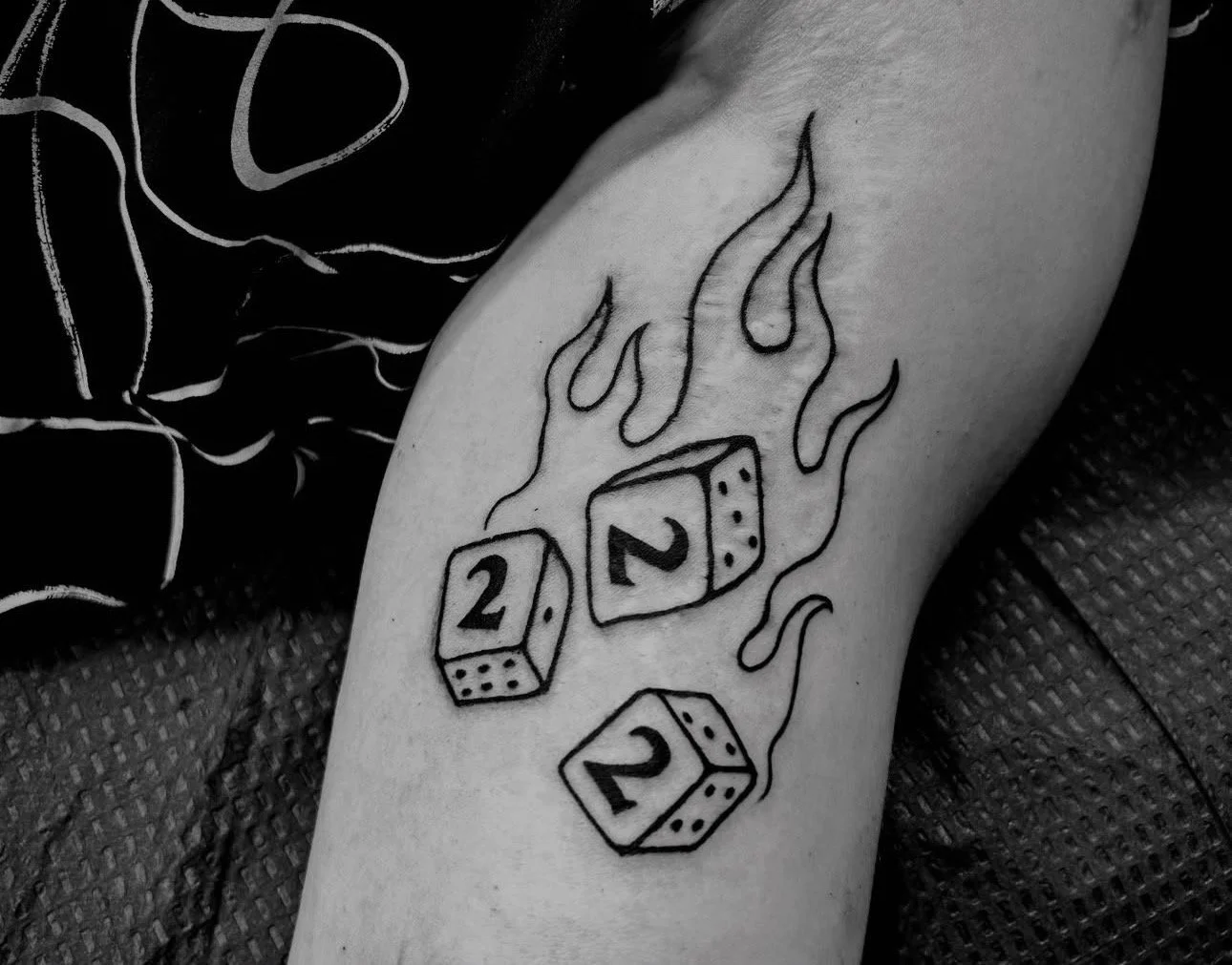 Tattoo of three dice showing two, two, and one, with flames around them.