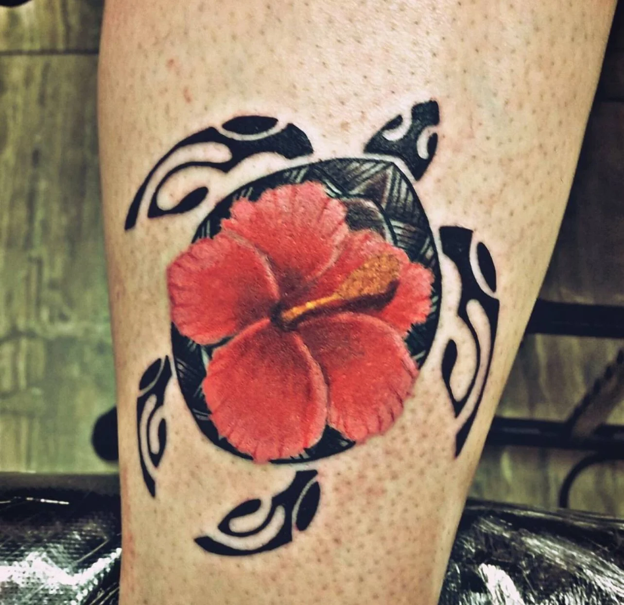 A tattoo of a red hibiscus flower with black outlines and background accents on a person's skin.