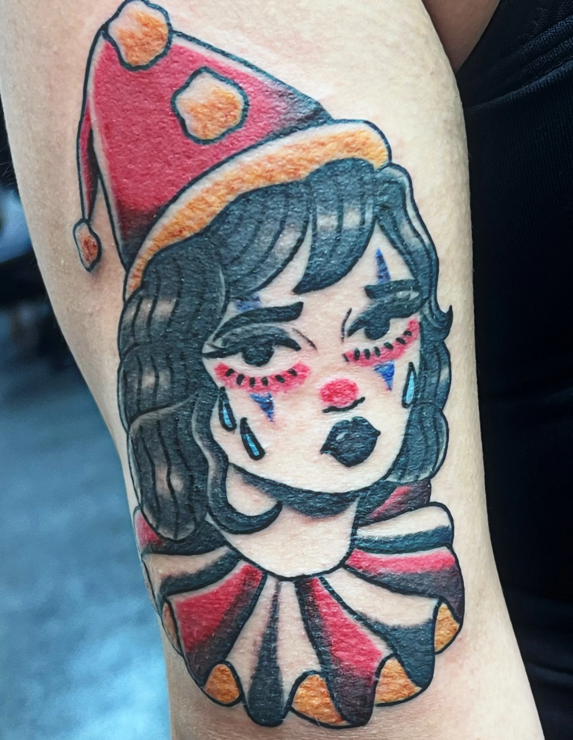 Colorful tattoo of a woman with black hair, red lips, and closed eyes. She is wearing a red outfit with orange dots and a matching bow on top of her head.