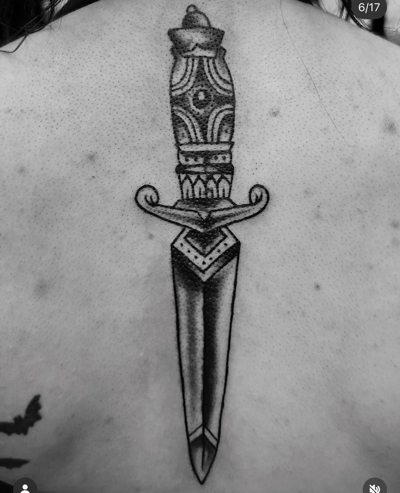 Black and gray tattoo of a double-edged sword with a decorative hilt, tattooed vertically down a person's back.