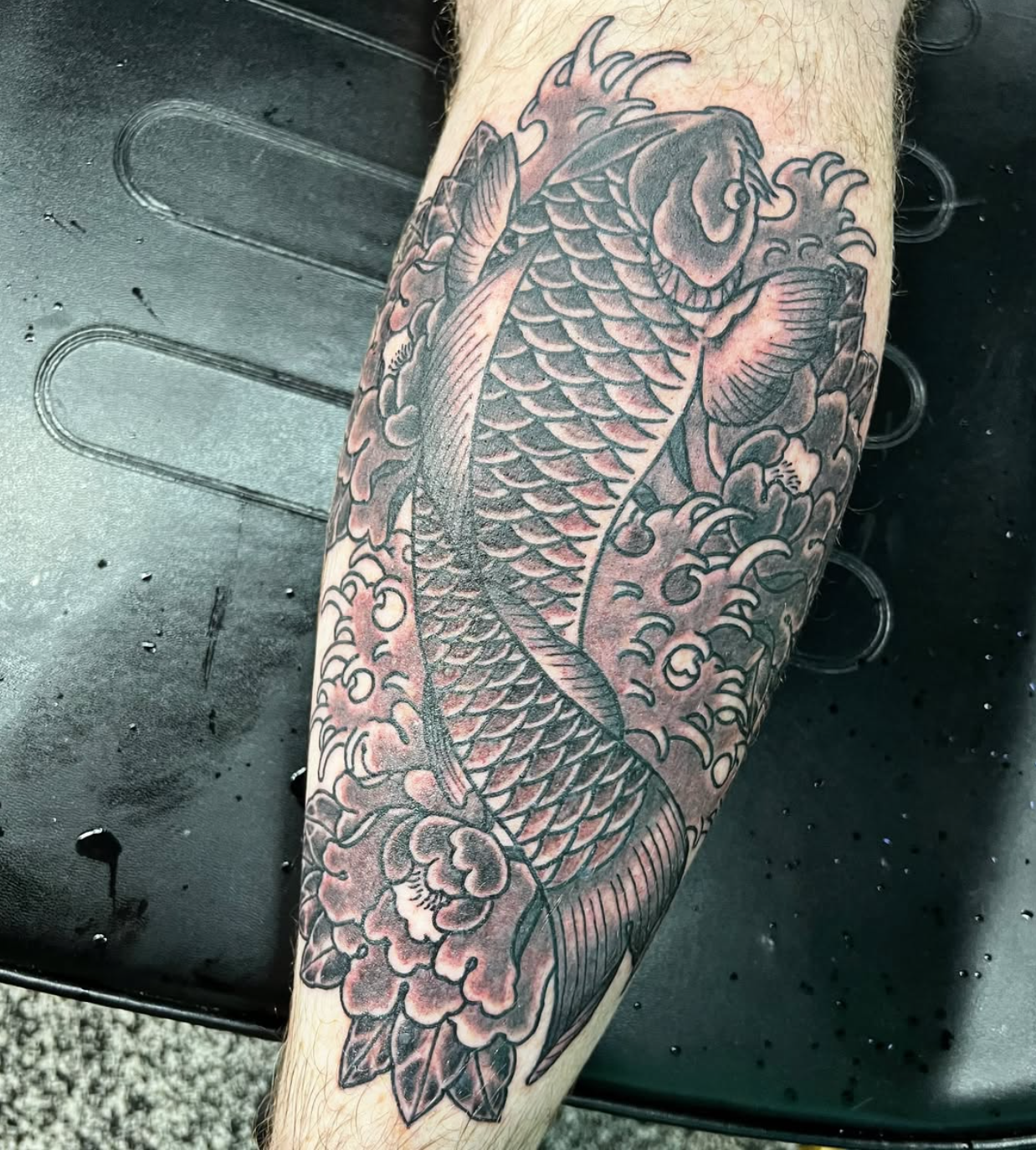 Black and gray tattoo of a dragon on a person's arm, featuring detailed scales, claws, and flowing smoke or clouds.