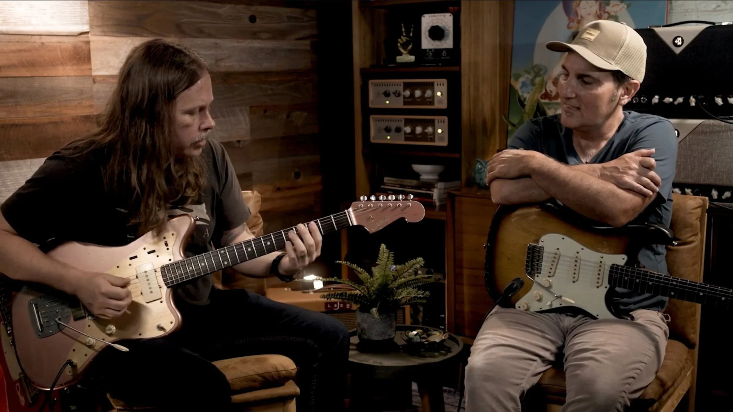 Justin Ostrander's Course - Sideman's Handbook with Brett Papa sitting on a couch in a music studio, one playing an electric guitar and the other holding an electric guitar, engaged in conversation.