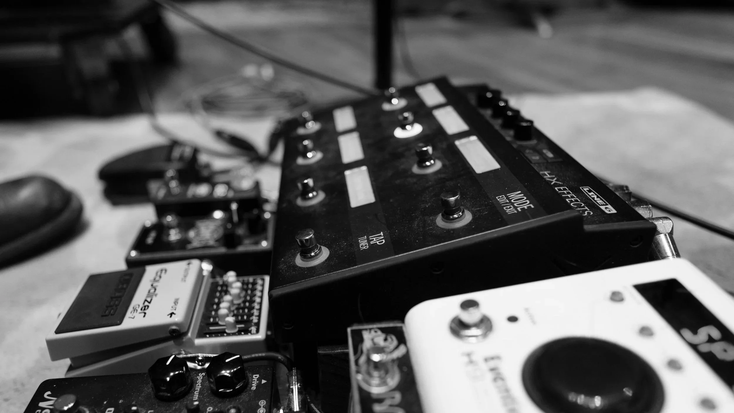 Justin Ostrander's Helix Close-up black-and-white photo of various guitar pedals and effects units arranged on a surface.