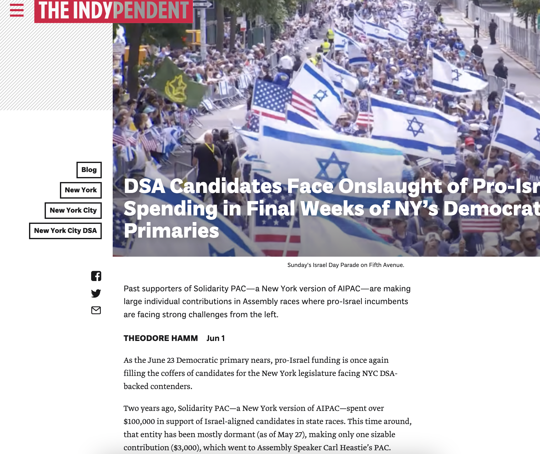 Crowd of people gathered on a city street for a parade, many waving Israeli flags and American flags, with some holding other flags and banners, lined with barricades and trees.