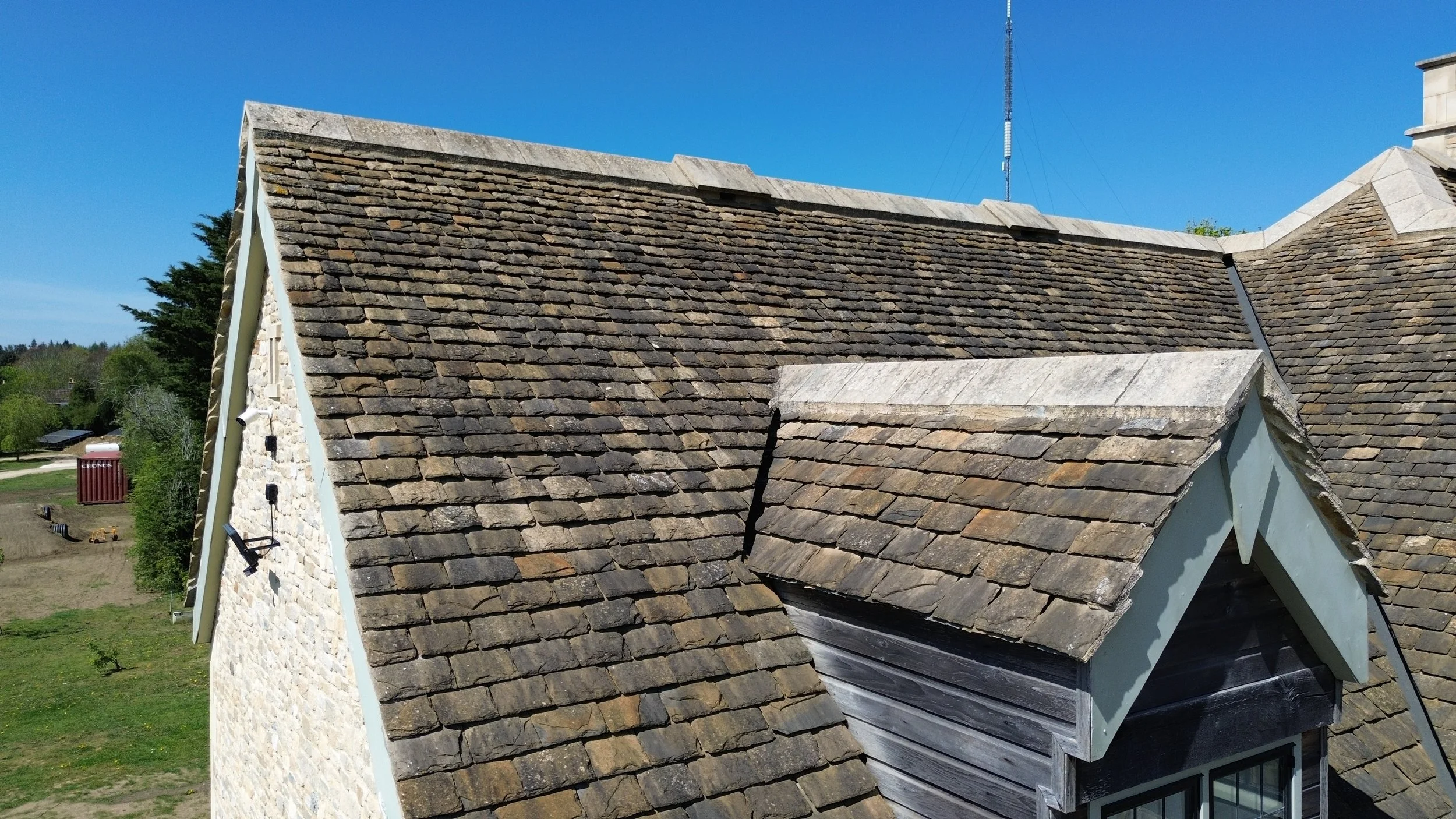 A close-up view of a stone-and-shingle roof on a house with cloudy eaves and surrounding trees.