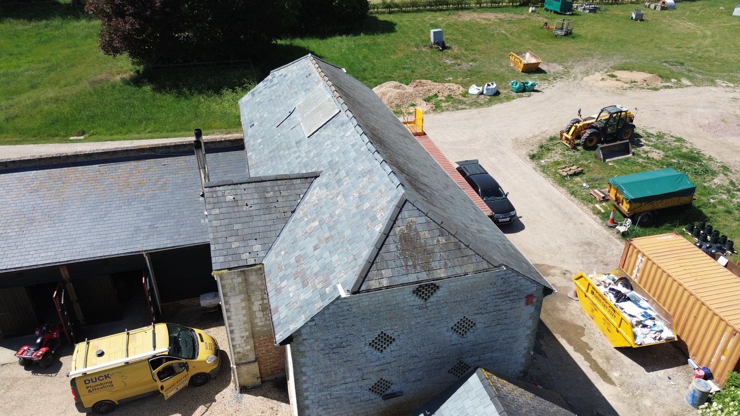 An aerial view of a construction or maintenance yard with a building, cars, construction equipment, and supplies.