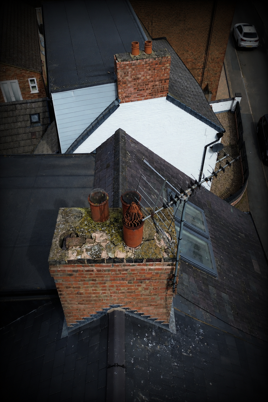 Aerial view of rooftop chimneys, antennas, and roof surfaces of residential buildings.