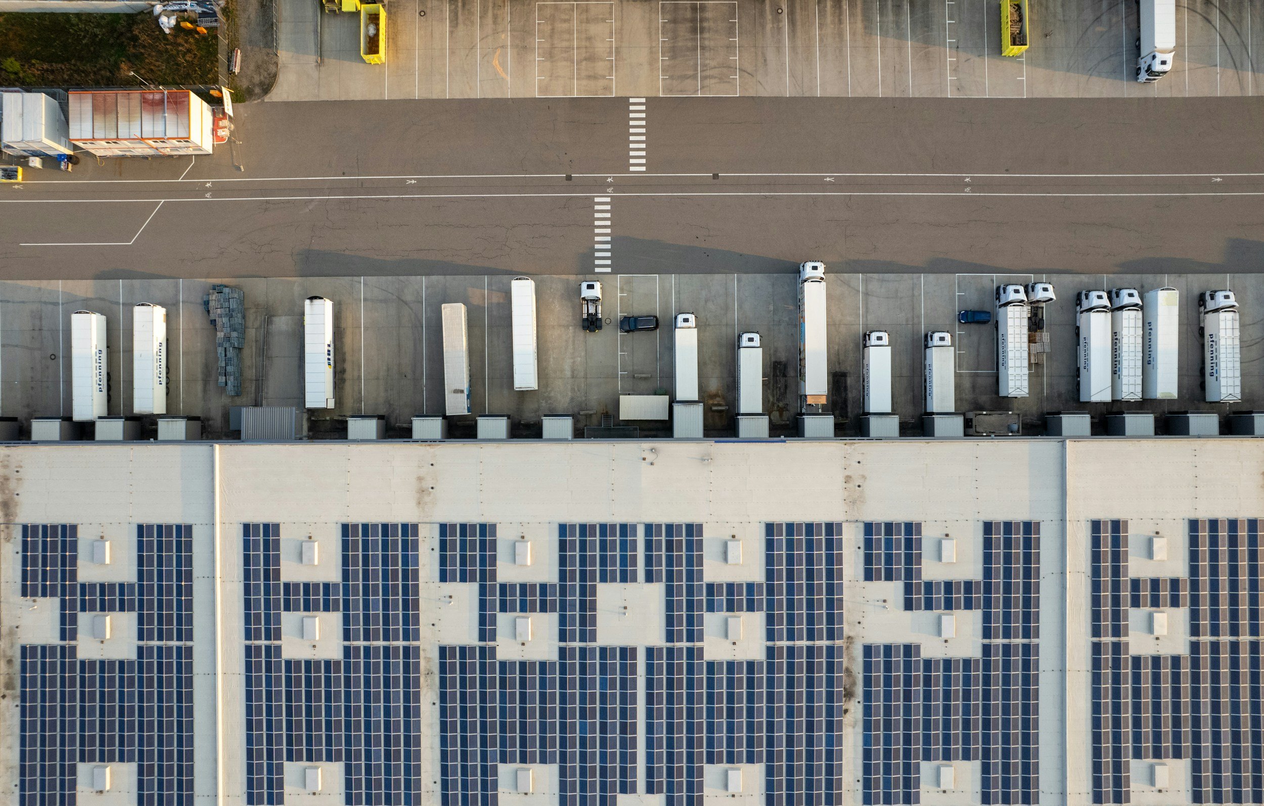An aerial view of a parking lot with trucks, cars, and a building with solar panels on the roof.
