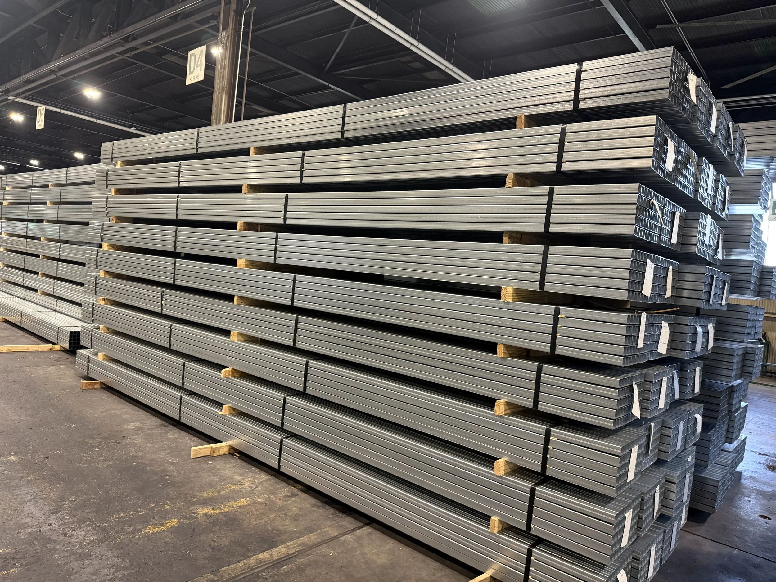 Stacks of metal tubing stored on wooden pallets inside a warehouse.