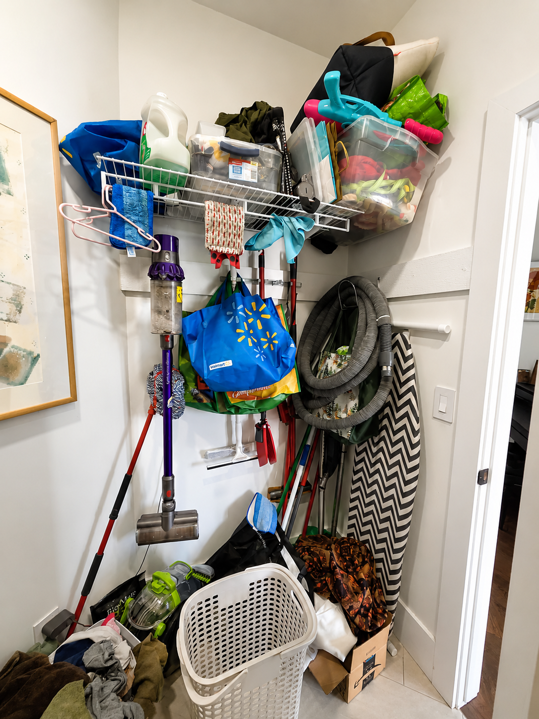 A closet or storage area filled with cleaning tools, bags, and miscellaneous household items stacked on shelves and the floor. Professional home organization in Saskatoon and area.