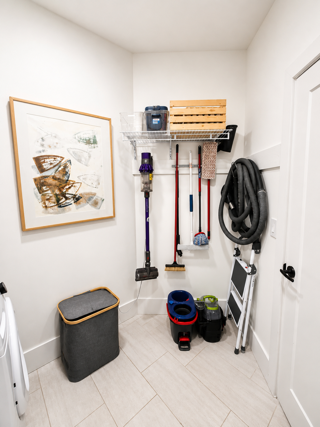 A small laundry or utility room with cleaning supplies and tools organized on the wall and floor, including a vacuum cleaner, mops, buckets, and a laundry basket. Professional home organization in Saskatoon and area.