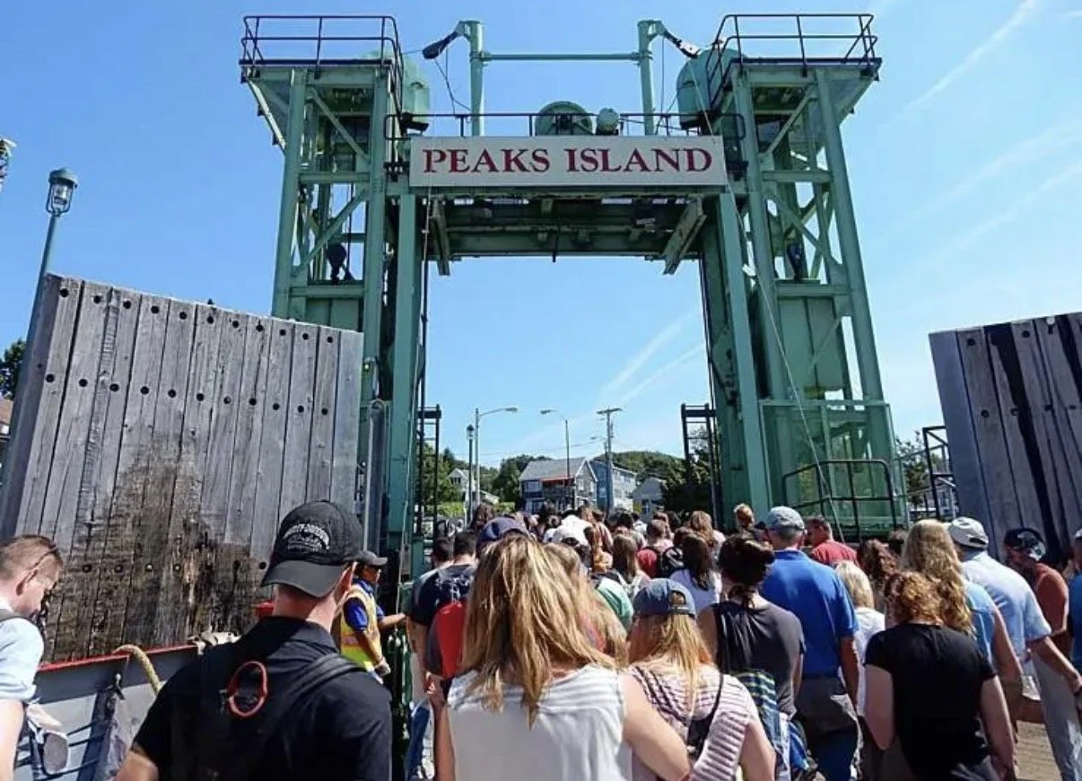 Crowd of people waiting in line at the entrance of Peaks Island, entrance sign visible above.