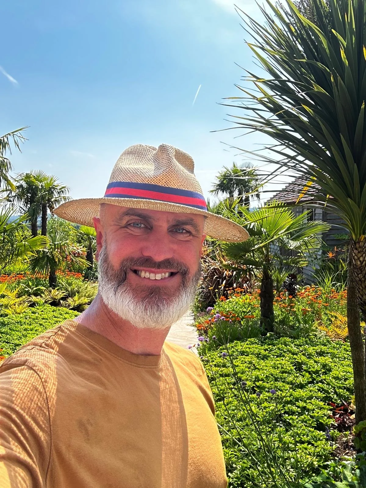 Joseph, the expert gardener also known as JP Gardens. With 30 years gardening experience. Joseph smiling in a beautiful and vibrant garden setting, with tall palms.