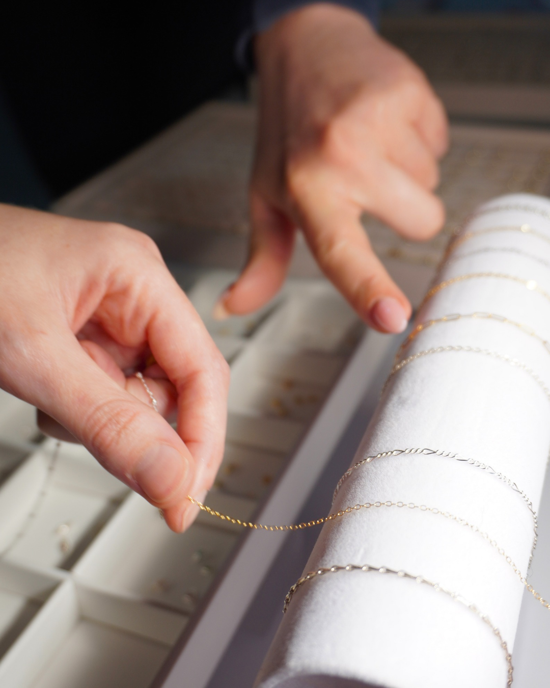 Close-up of hands arranging delicate gold chains on a white jewelry display roll.