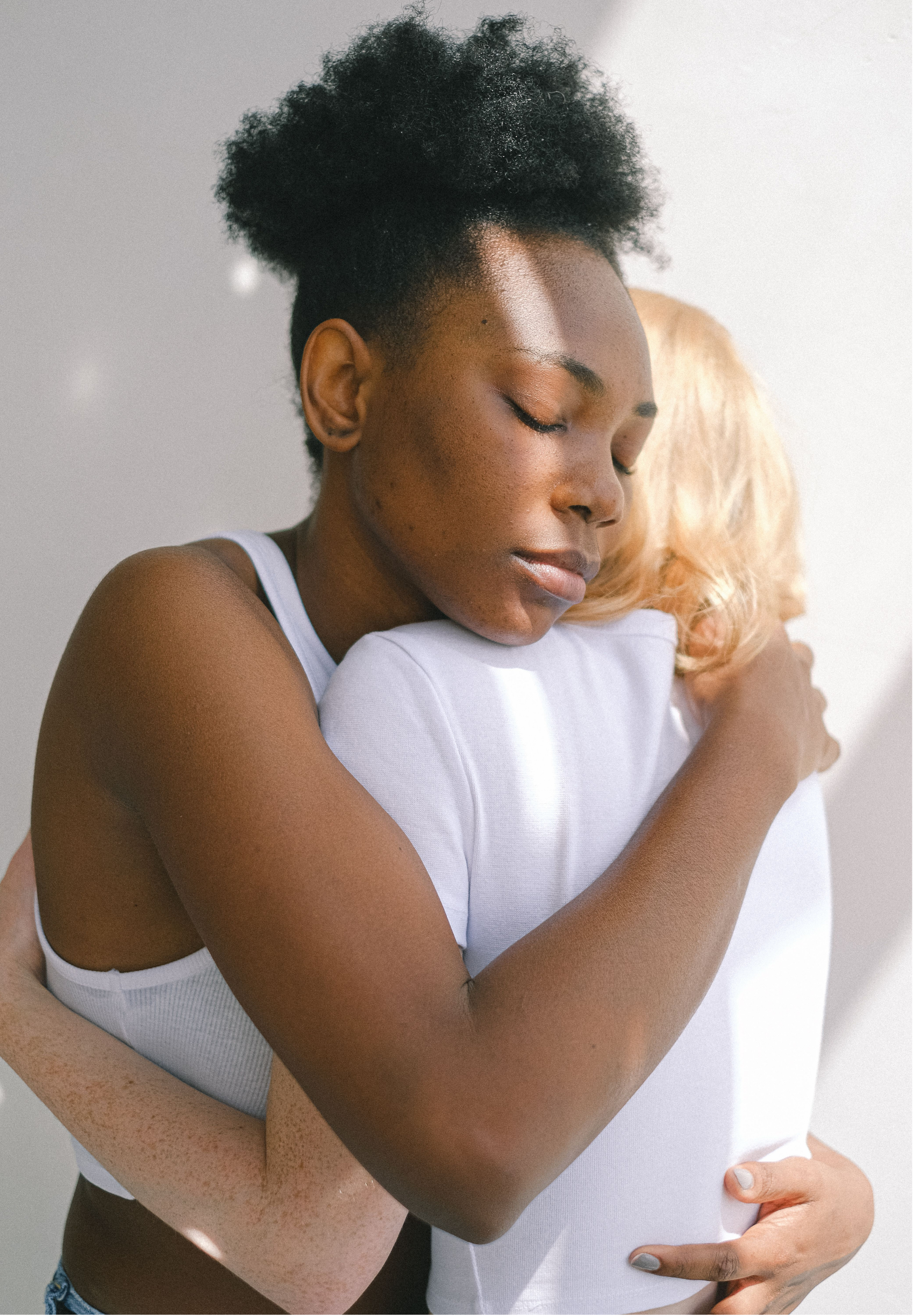 Close-up of two women embracing, with one woman's face resting against the other's shoulder and eyes closed.