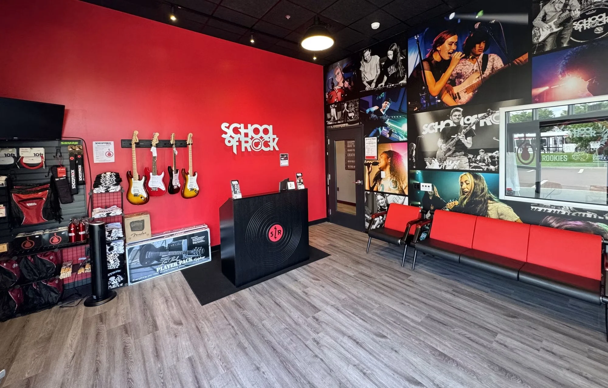Music store with guitars on display, stage photos on the wall, posters of musicians, a red bench, and a reception counter.