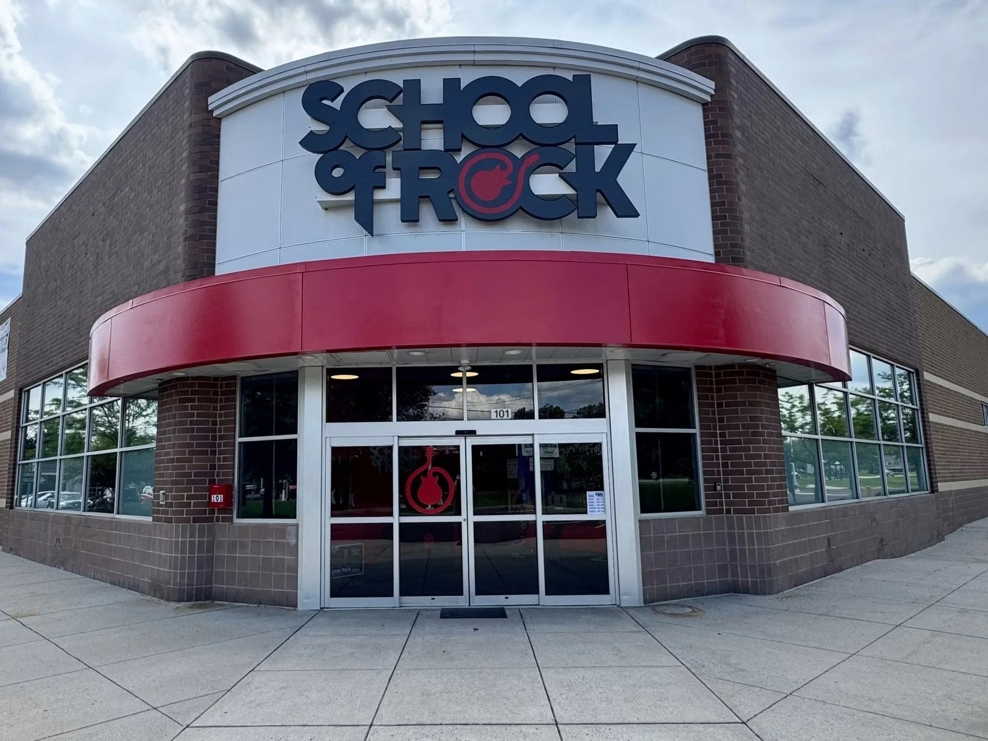 Front of School of Rock building with a large sign displaying the school name and logo, featuring a stylized red guitar pick.