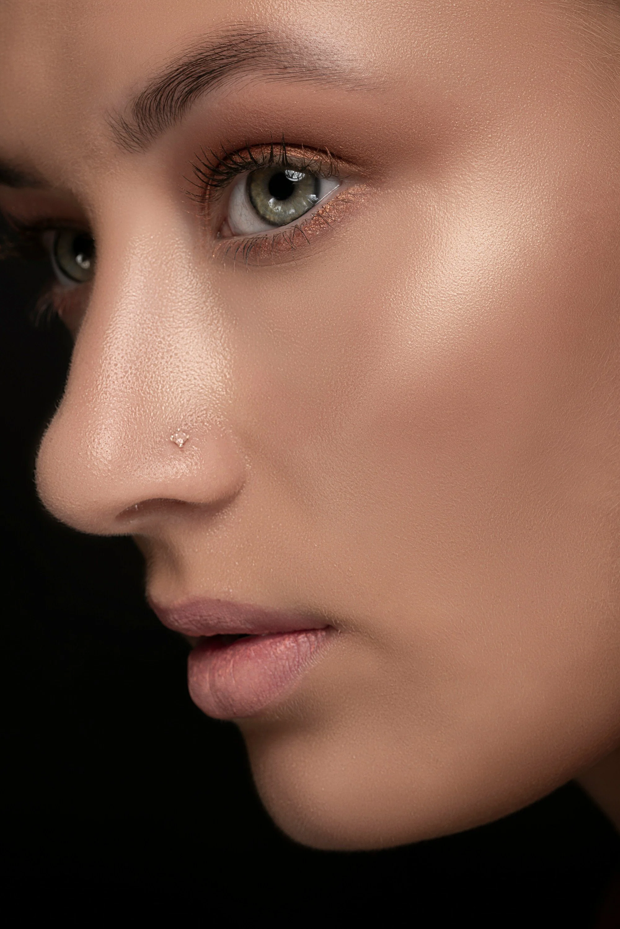 Close-up of a woman's face, focusing on her green eye, well-defined eyebrow, and smooth skin with a dark background.