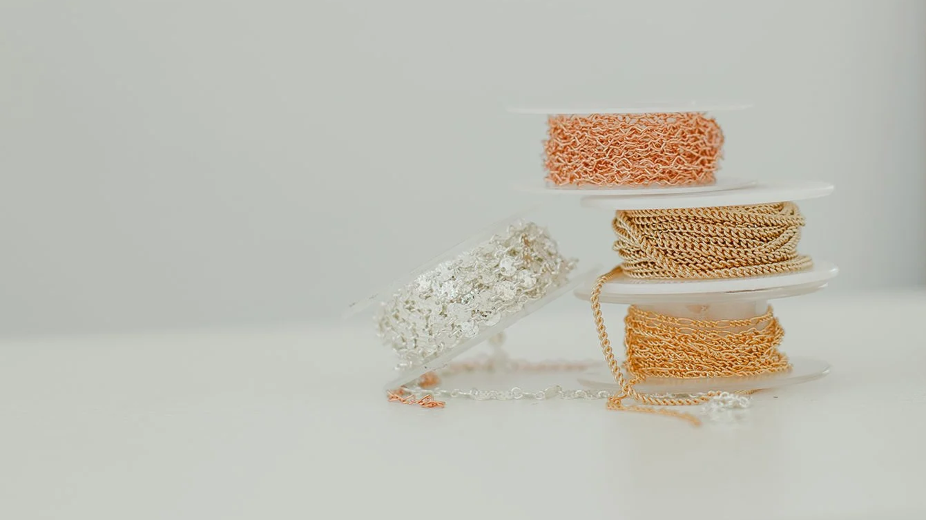 Stack of white and gold jewelry, including chains and a choker, on white display trays against a plain background.