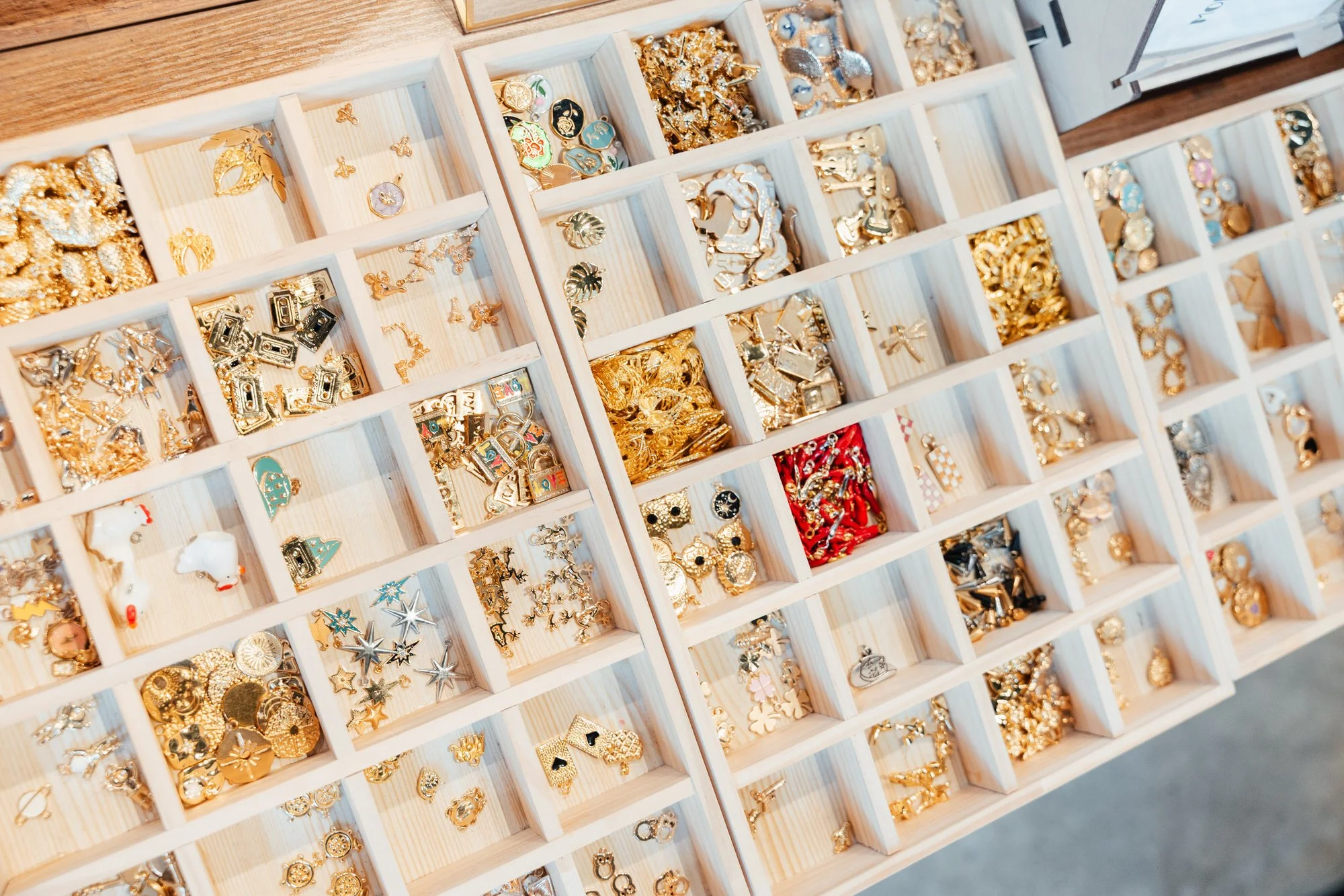 A wooden jewelry display box containing multiple compartments filled with various gold and silver earrings, rings, and charms.