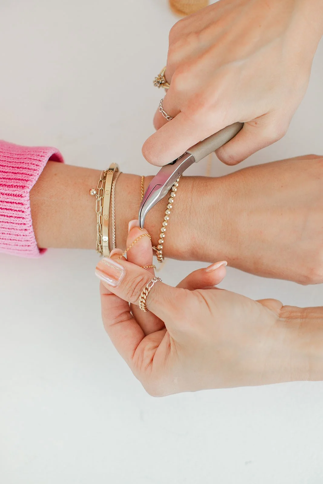 Person using a cuticle remover tool on their fingernail with multiple rings and bracelets.