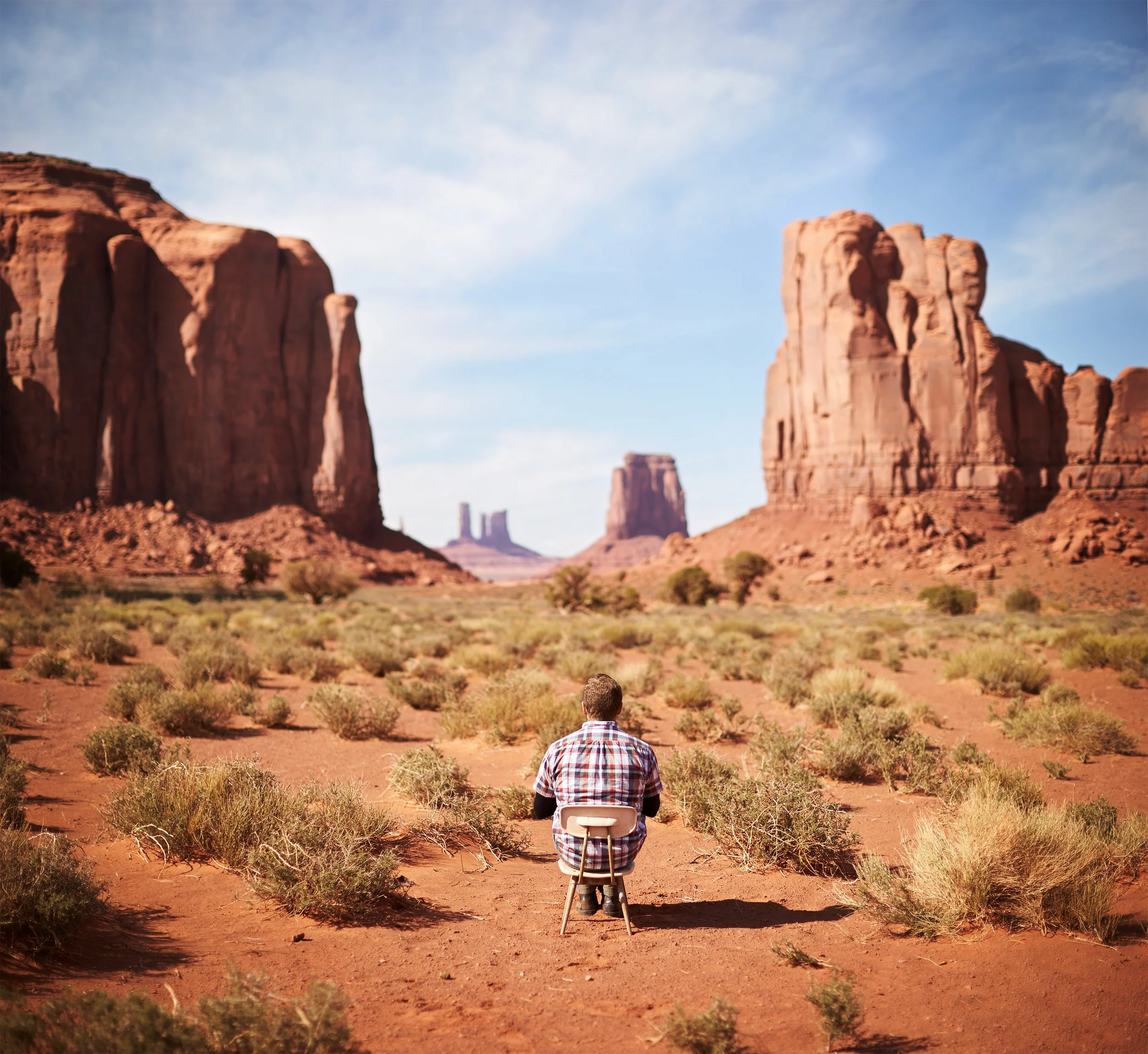 A person sitting on a chair in the desert, facing large red rock formations under a blue sky. Andrew Fornasier Digital Tech San Francisco