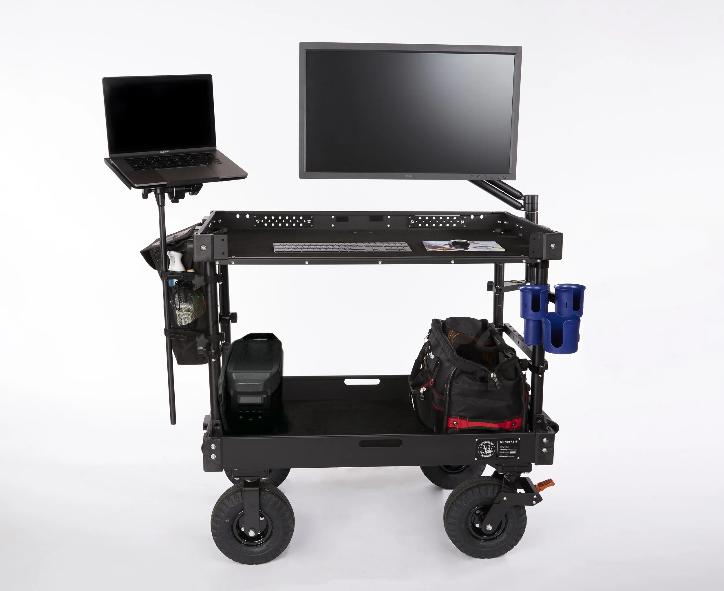A mobile workstation with a mounted monitor and a small laptop on a stand, equipped with various storage compartments, tools, and accessories on a black metal frame with wheels. Andrew Fornasier Digital Tech San Francisco