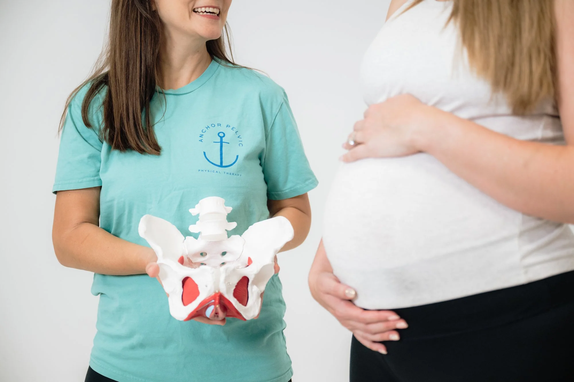 a pelvic therapist holding a pelvis model and working with a woman with a pregnant belly
